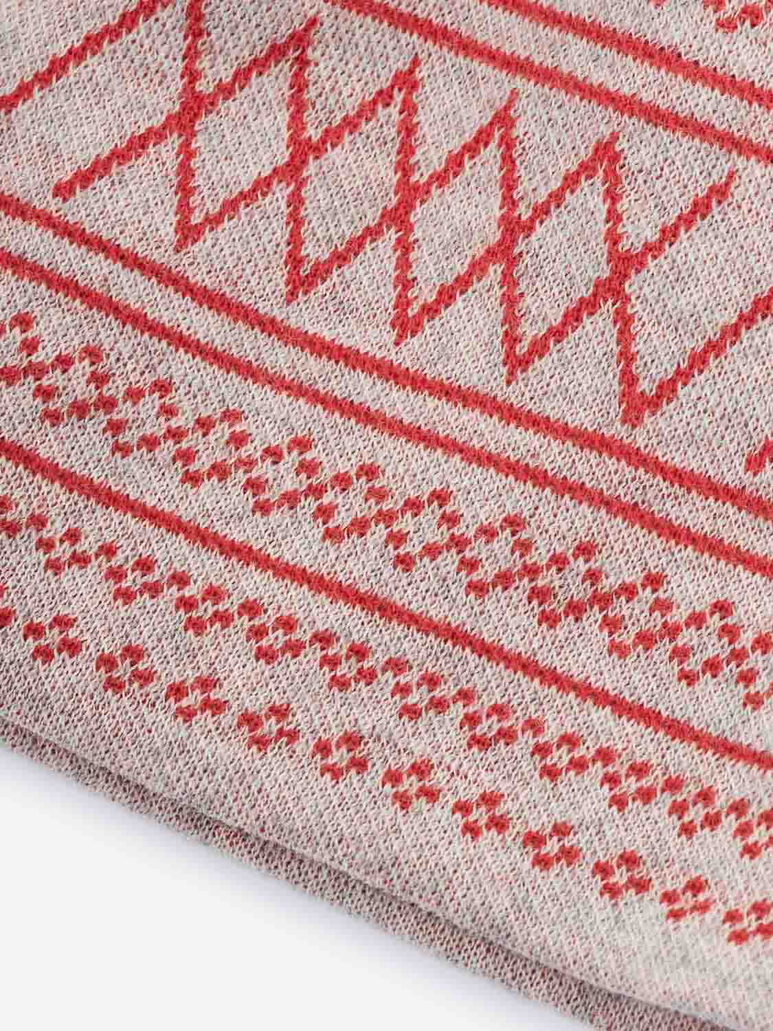 Close-up of a fabric from We Norwegians' Setesdal Hat Cream, showcasing intricate red geometric and floral patterns on a beige background, crafted from luxurious Italian yarn. The design features rows of diamonds and small cross motifs, reminiscent of the classic Setesdal hat.