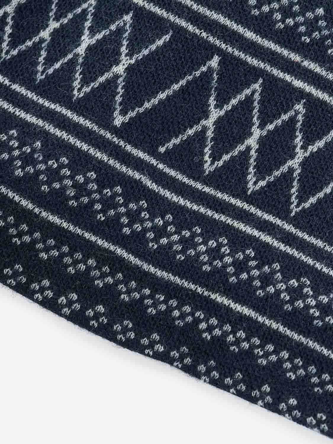 Close-up of a jacquard fabric from We Norwegians' Setesdal Hat Navy/Off White, showcasing a white geometric pattern. The design includes diagonal lines creating diamond shapes and small circular motifs in rows, echoing the intricate textures typical of traditional Setesdal hats.
