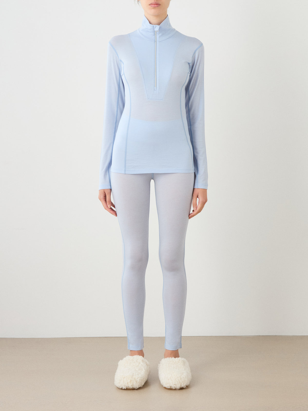 A person wearing a Sno Merino Zip Up Women quarter-zip top and matching leggings with fluffy white slippers.