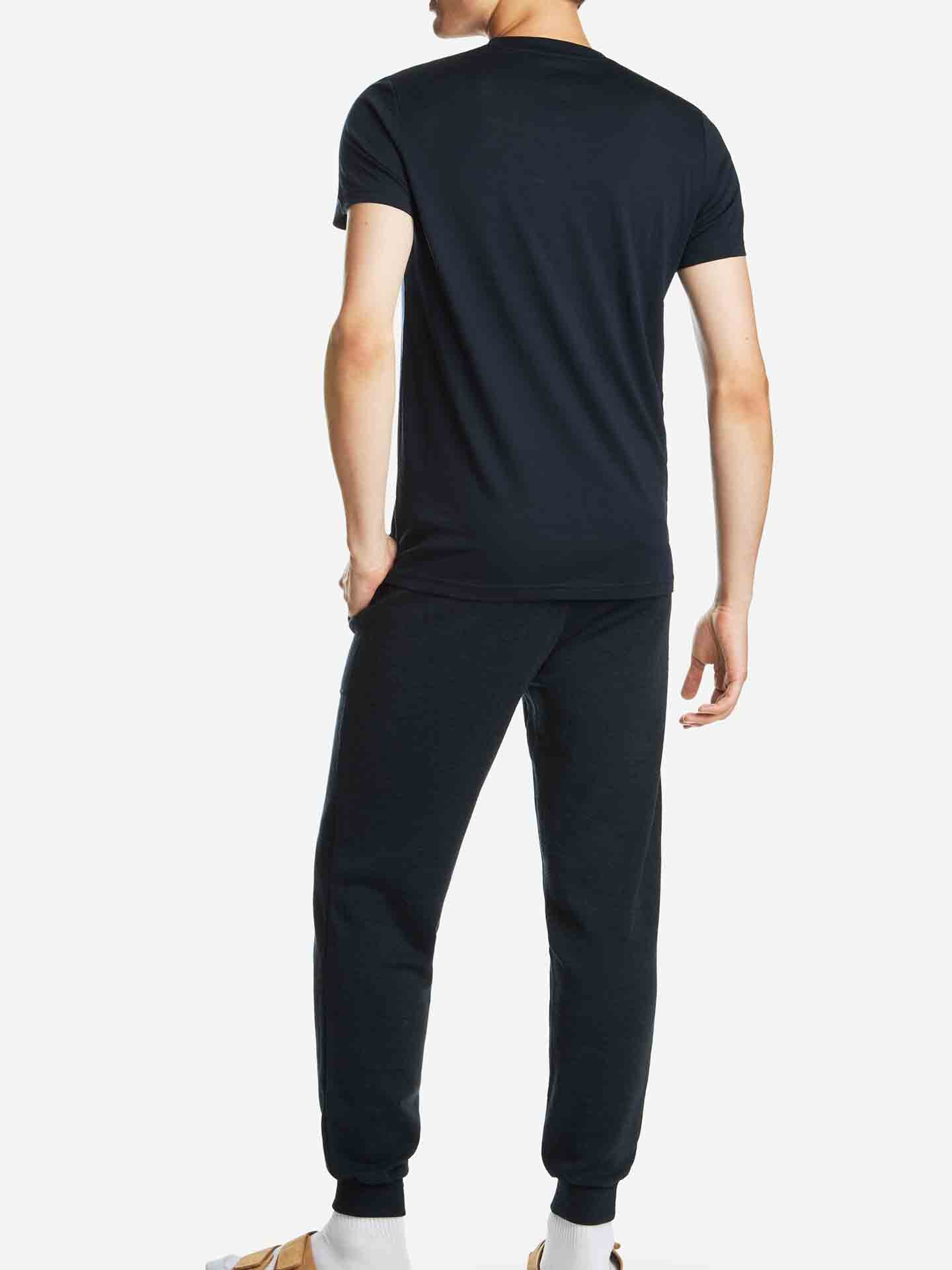 A person is seen from the back, wearing a matching navy Base One Pocket Tee by We Norwegians and black joggers. They have one hand in their pocket and are standing on a white background, wearing white socks and brown slippers.
