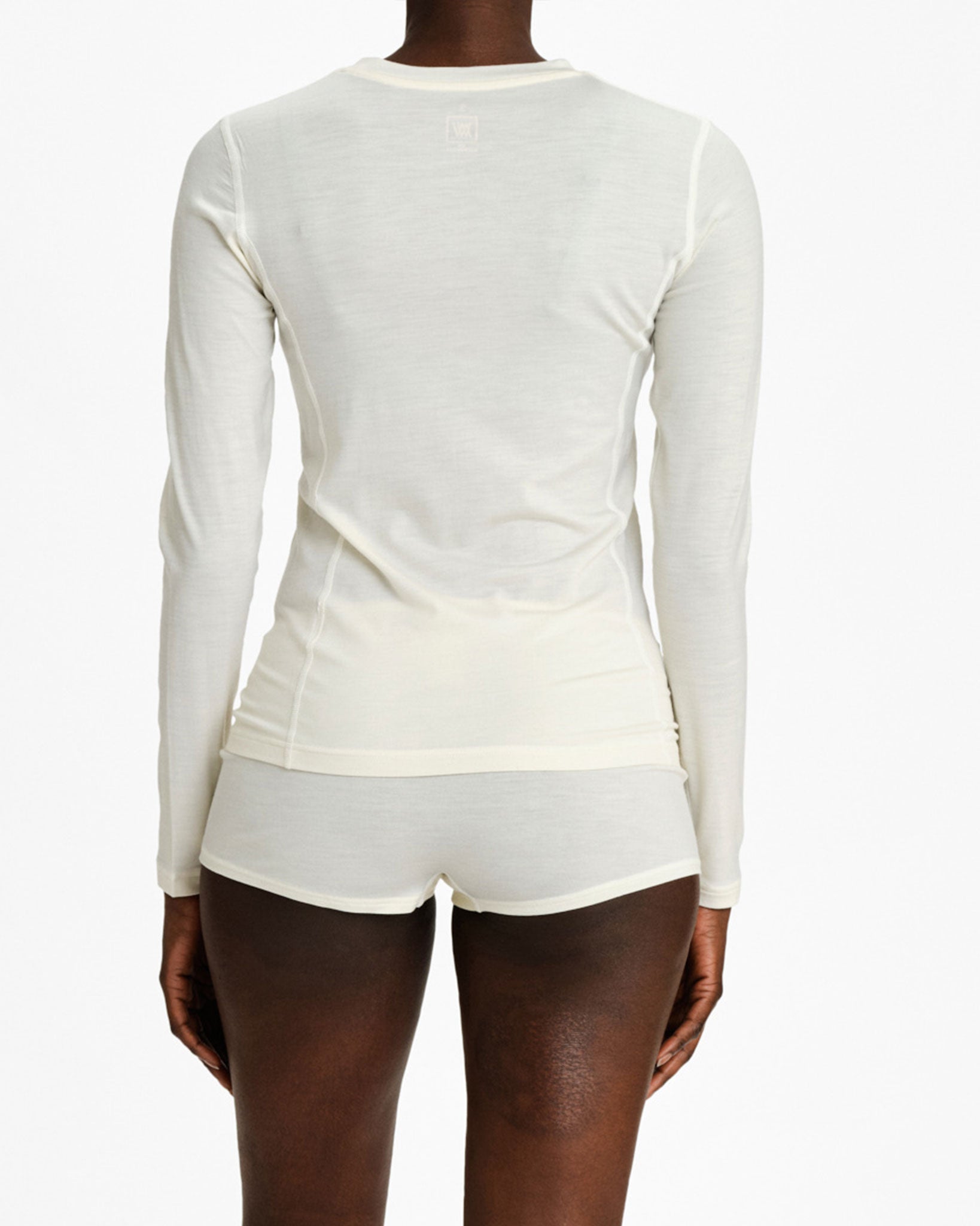 Rear view of a person wearing the Sno Merino Crewneck Women and matching shorts from We Norwegians, crafted from super fine merino wool. The plain white background emphasizes the Scandinavian luxury base layers and highlights the exquisite fabric texture with a slightly fitted top.