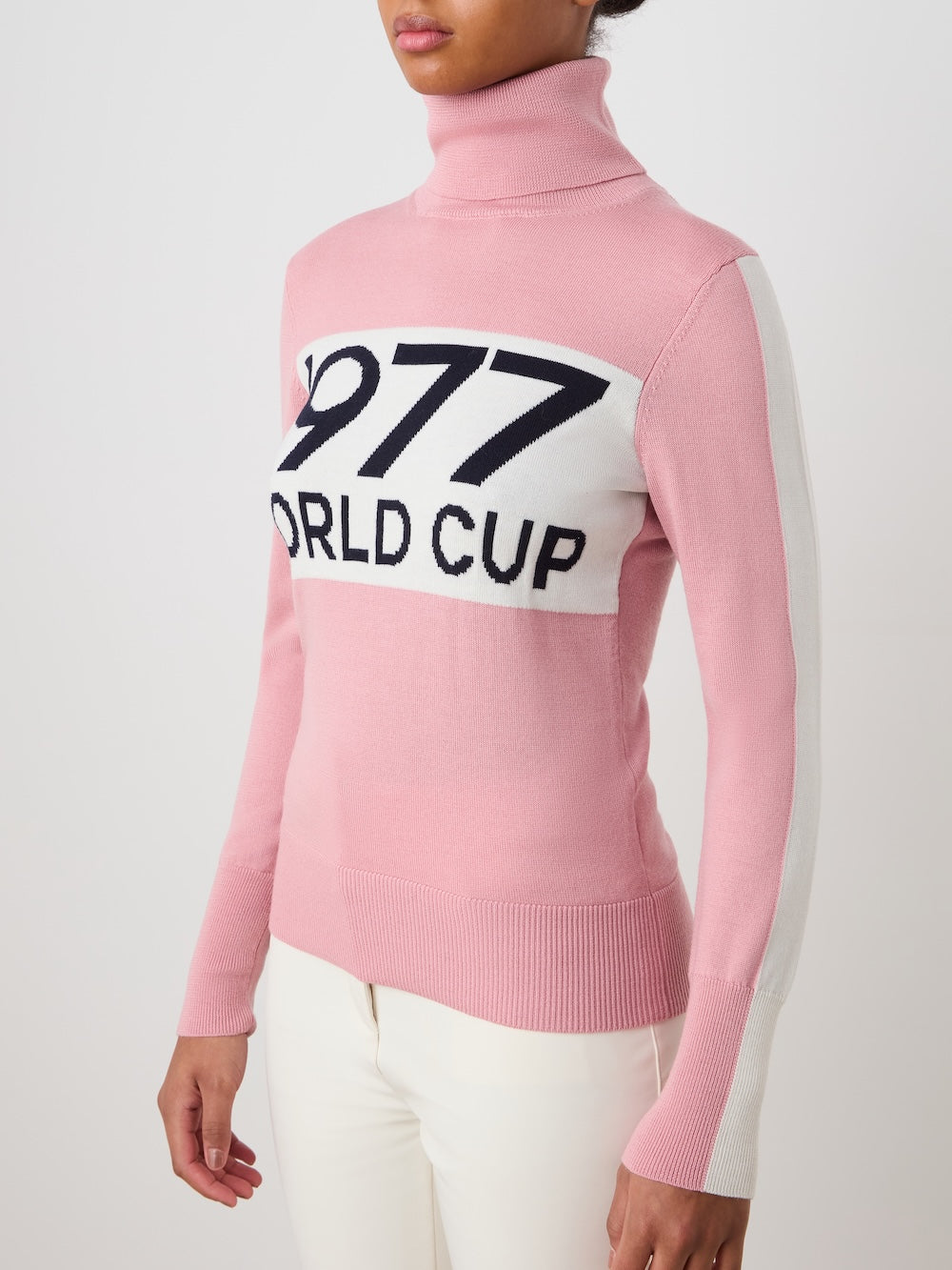 A woman wears the We Norwegians World Cup Sweater women - Pre Spring 26, featuring "1977 WORLD CUP" on the chest, styled with white pants against a plain background.