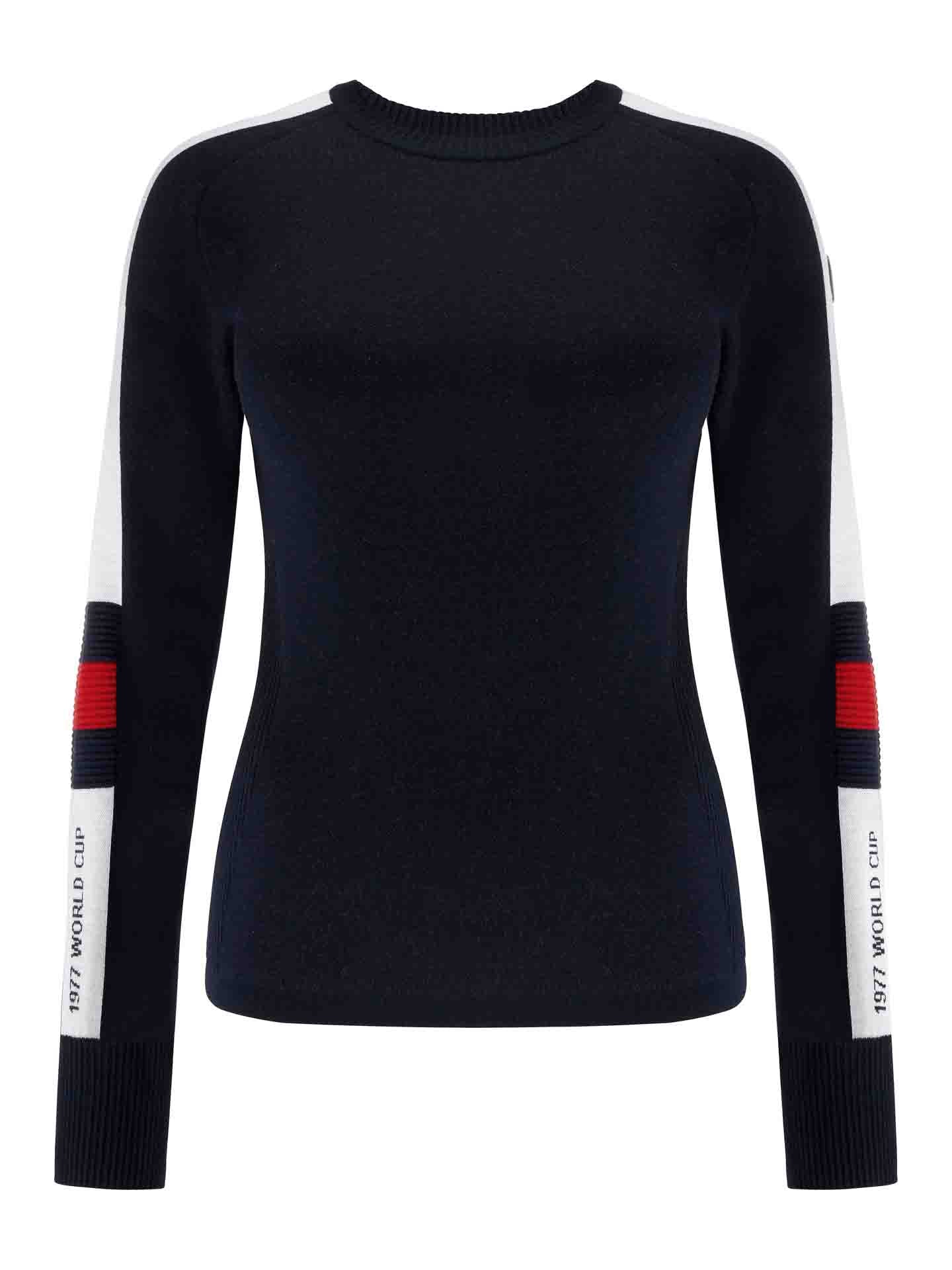The Hafjell Crewneck Women Flag sweater by We Norwegians is a form-fitting, long-sleeved black ski sweater featuring white and red vertical stripes on the upper arms. The left sleeve has "1977 WORLD CUP" text in white near the cuff. This crewneck sweater is made from fine merino wool, with ribbed neck and cuffs for added comfort.