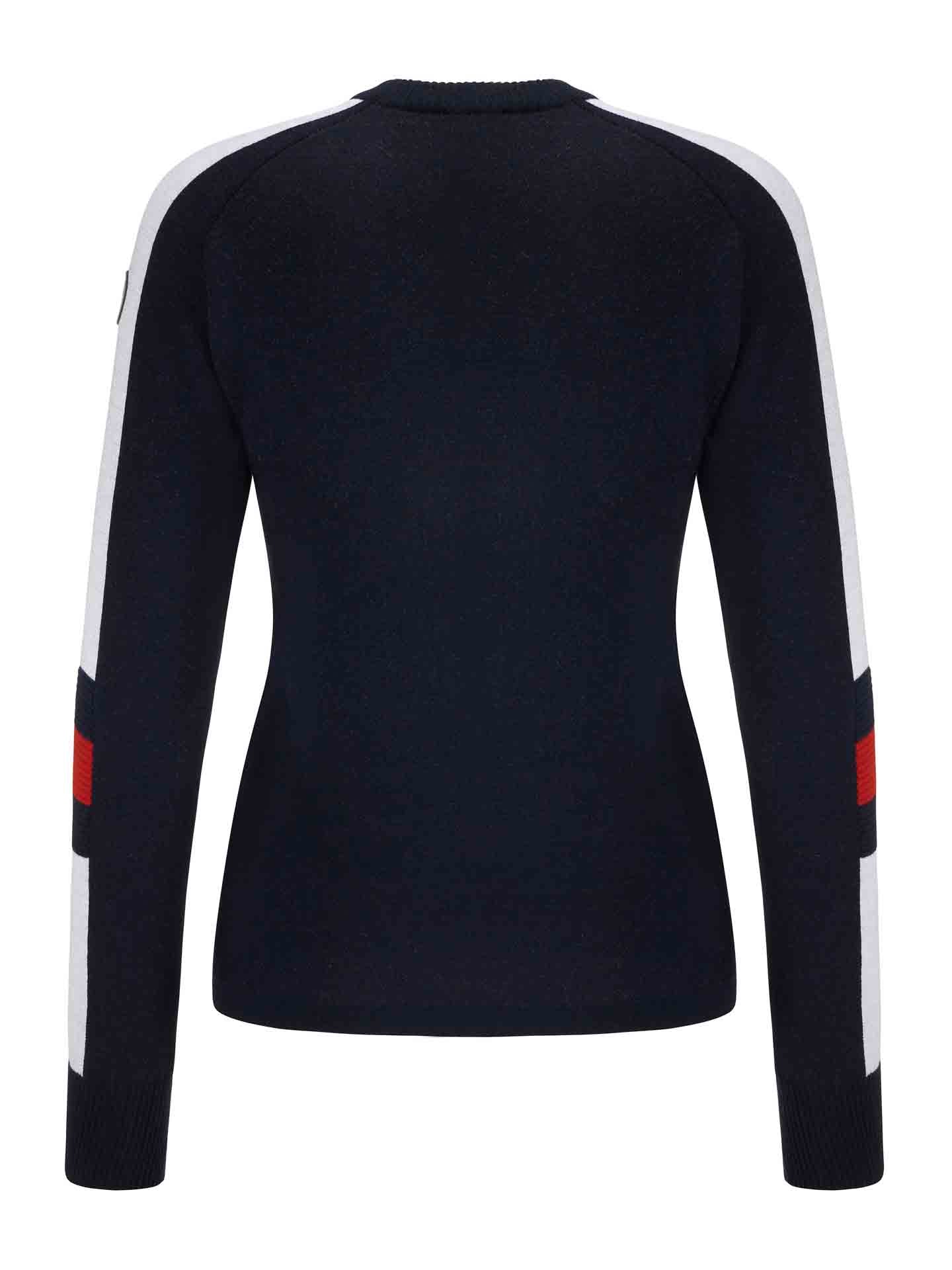 The Hafjell Crewneck Women Flag by We Norwegians is a navy long-sleeve top with a snug fit, crafted from fine merino wool. The sleeves feature wide white stripes running from the shoulders to the cuffs, interrupted by a red block on the upper arm. The back view showcases the simplicity of this ski sweater's design.