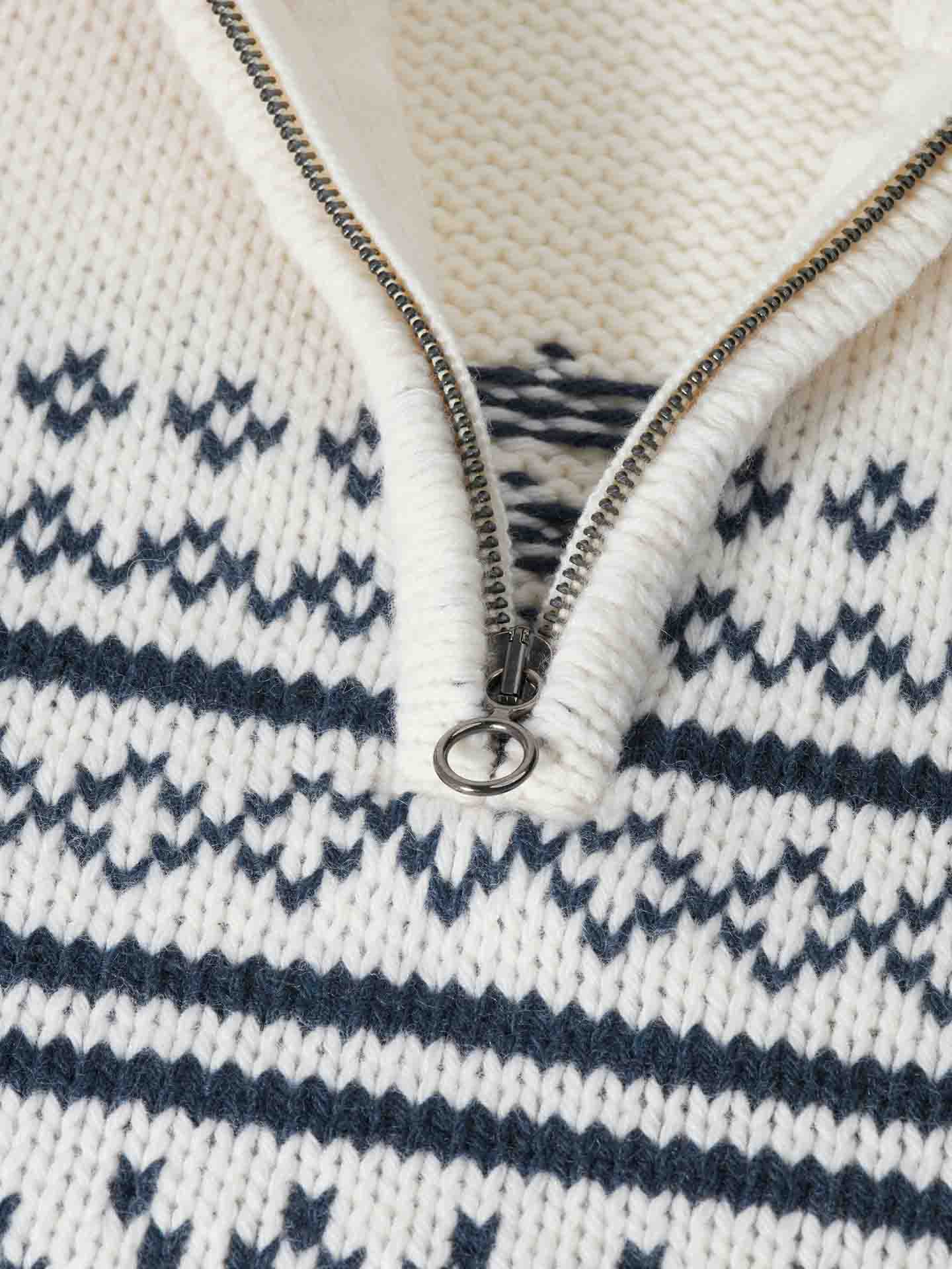 Close-up of the Setesdal Zip Up Sweater Men Off White by We Norwegians, featuring a white merino wool knit with a black geometric pattern and a half-zipper adorned with a round metal pull. The texture of the knit fabric and detailed design are clearly visible, with the zipper partially open, highlighting more of the chic après ski style underneath.