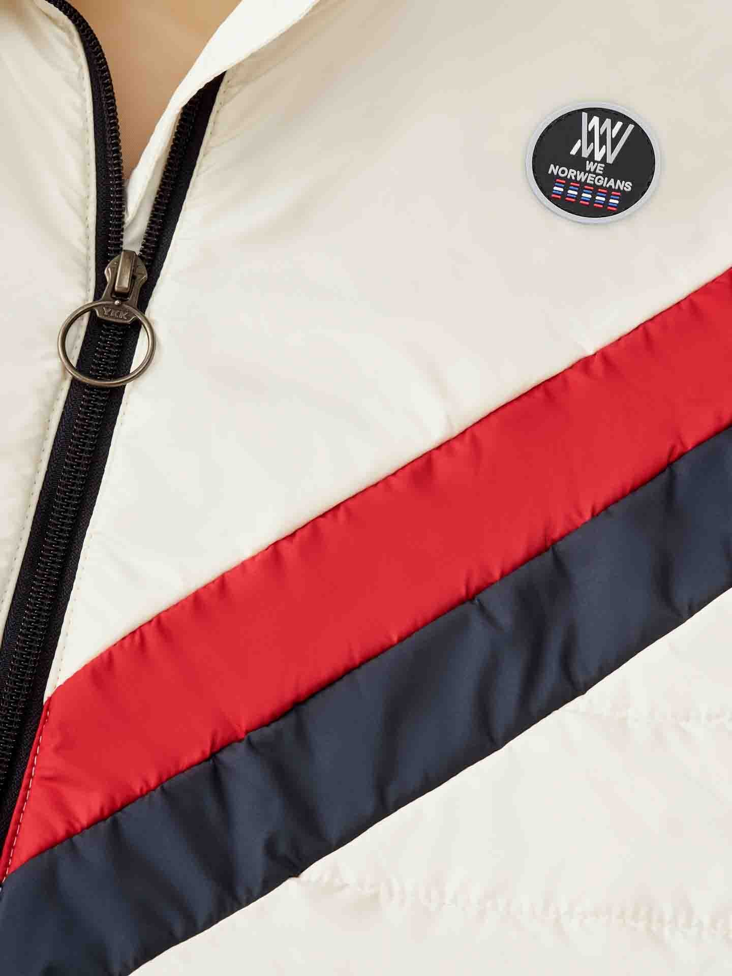 Close-up of a Myrken Lavalan Vest for men in white by We Norwegians, showcasing diagonal color blocks in red and black. A zipper with a round pull is visible, along with a small, circular "We Norwegians" logo patch near the chest area. The lightweight, quilted fabric features water repellent properties and wool filling for added warmth.