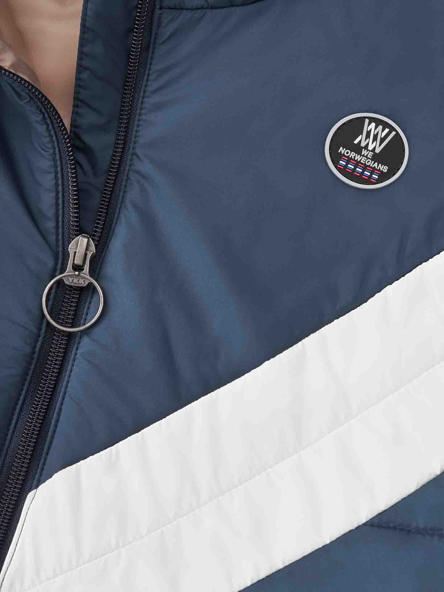 Close-up of a person wearing a navy and white We Norwegians Myrken Lavalan Vest Men, featuring a round silver zipper pull. The vest, crafted from water repellent fabric, showcases an emblem with the text "We Norwegians" in the top right corner.