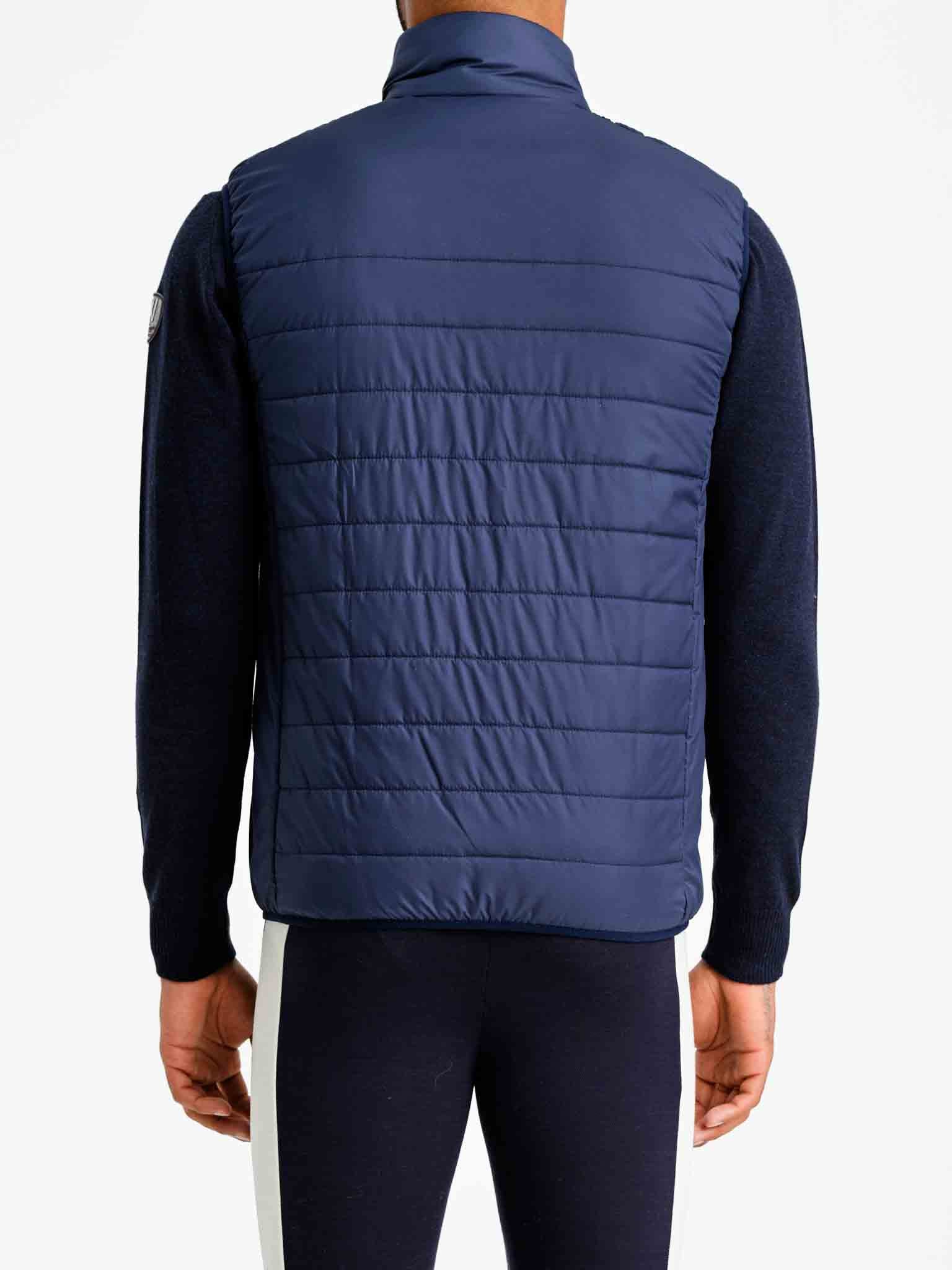 A person is shown from the back wearing a We Norwegians Myrken Lavalan Vest Men Navy over a long-sleeved dark shirt. They are also wearing dark pants with a white stripe down the side. The background is plain white.