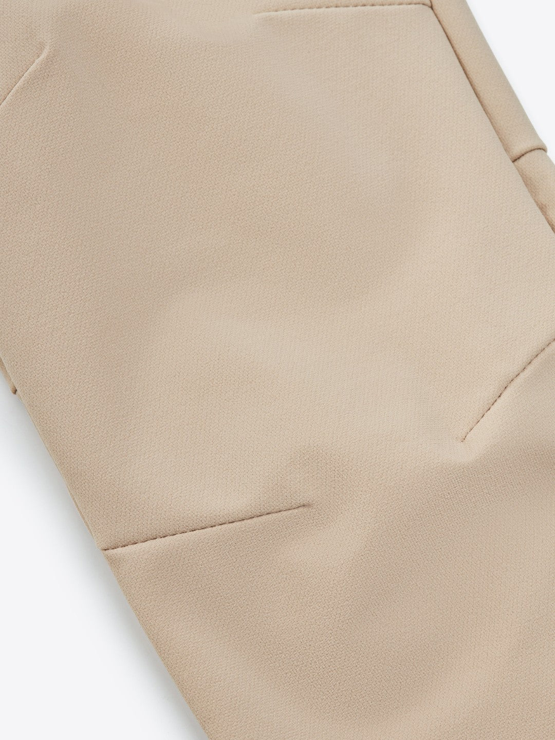 A close-up image of the We Norwegians Lista Pant Women Sand, a beige garment that could be trousers. The smooth fabric features visible stitching and seams that create geometric patterns for a tailored appearance. Made from Swiss Schoeller fabric, the design is minimalistic and clean while offering the comfort of 4-way stretch.