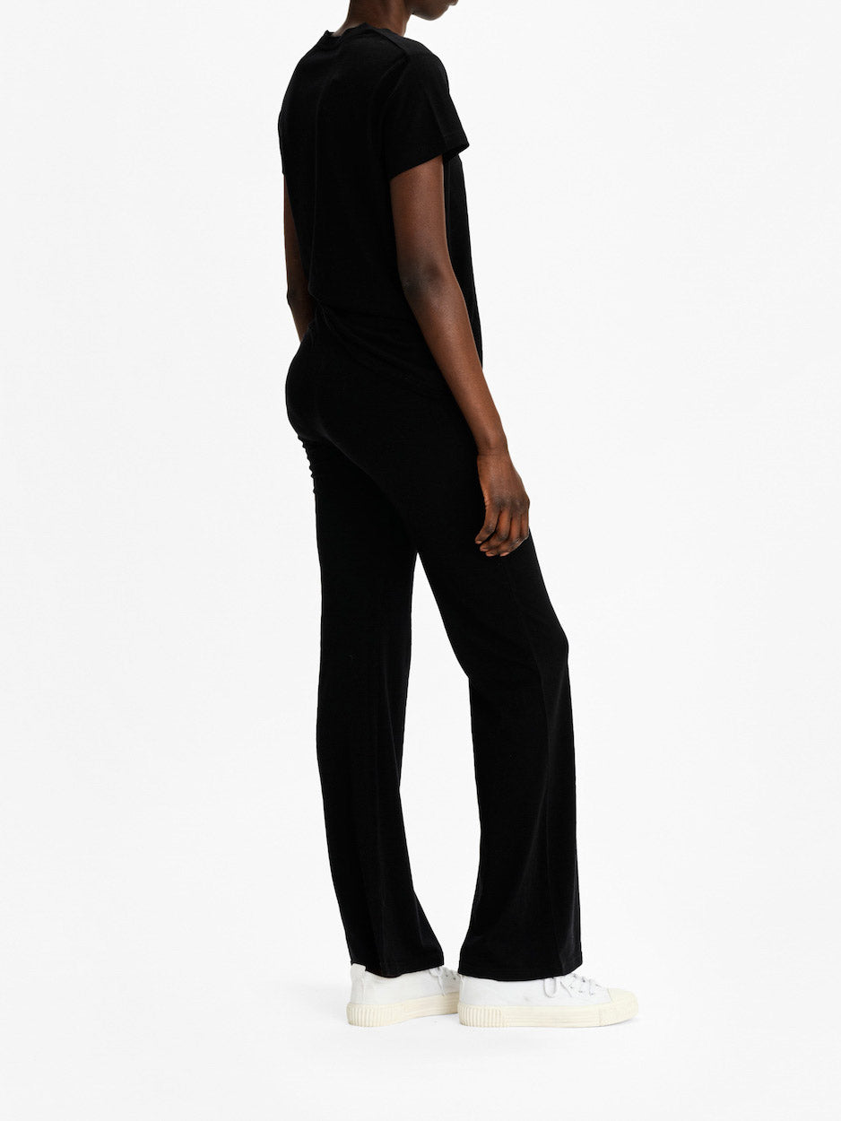 A person wearing a "Salt Classic Top Women Black" by We Norwegians and matching black pants, reminiscent of Scandinavian Luxury Essentials, is standing on a white background. They are also wearing white platform sneakers. The person is viewed from the side and slightly from the back.