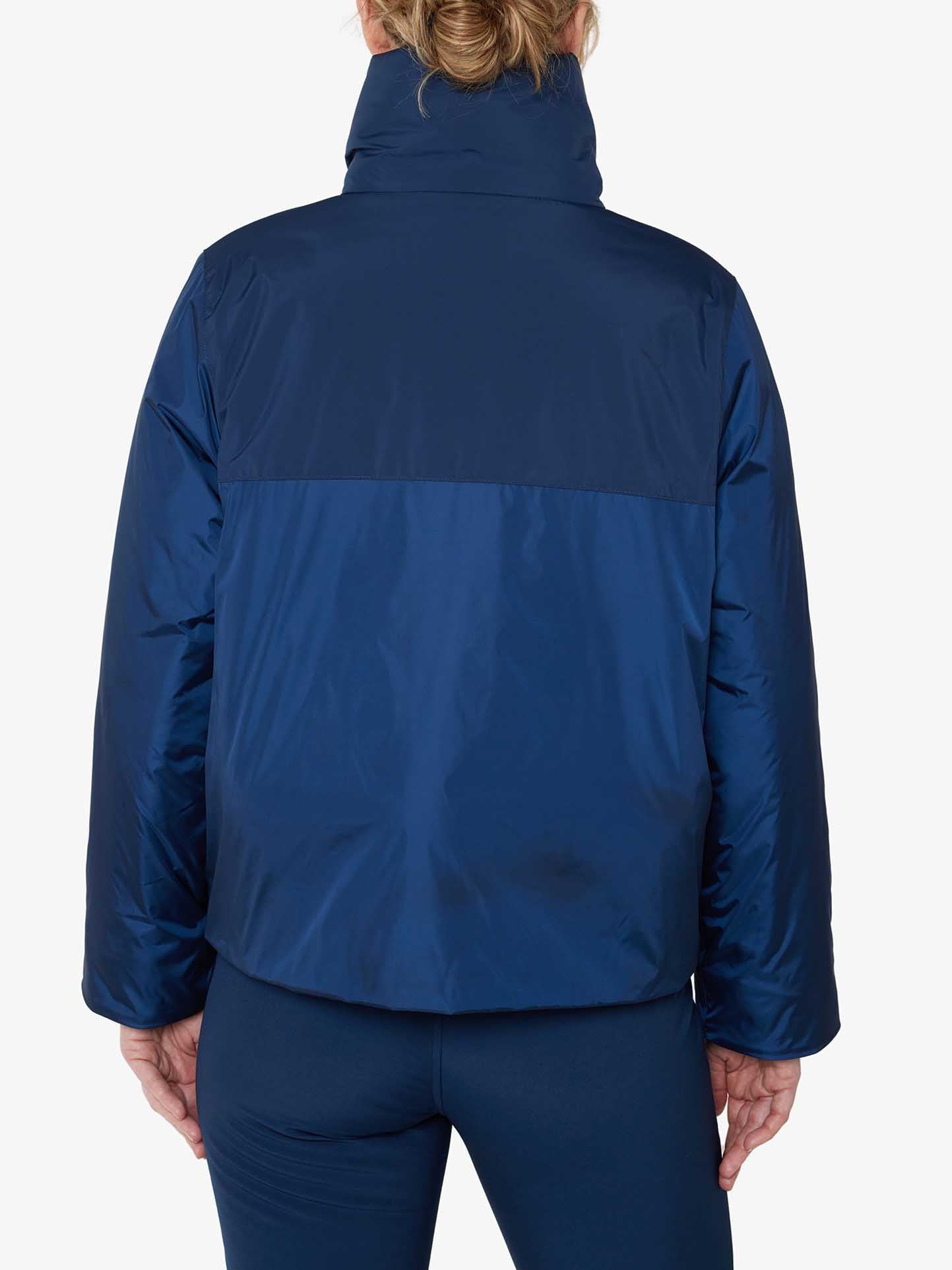 A person with light hair is shown from the back, wearing the We Norwegians' Filefjell Ski Jacket Women in dark blue, which boasts a high collar. This puffy jacket features wool padding that offers warmth and protection against the cold. The individual is also sporting navy blue pants, set against a plain white background.