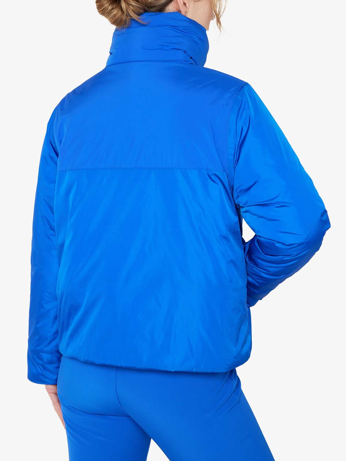 A person wearing a We Norwegians Filefjell Ski Jacket Women in royal blue, along with matching blue pants, is seen from the back. The high-collared, water-repellent ski jacket has the person’s left hand resting on their hip against a plain white background.