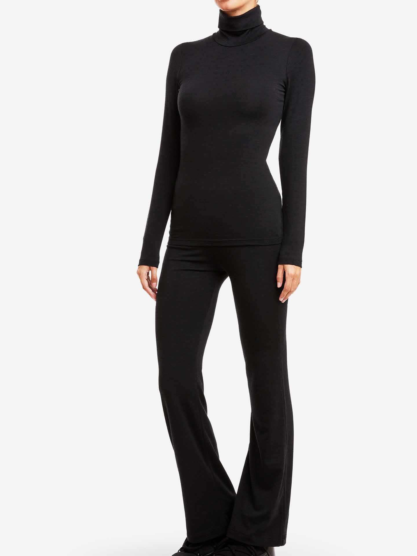A person wearing a black We Norwegians Hygge Turtleneck Women and black flared pants is shown from the neck down. The outfit, crafted with HYGGE base layer precision, is monochrome and fitted. The background is plain and white.