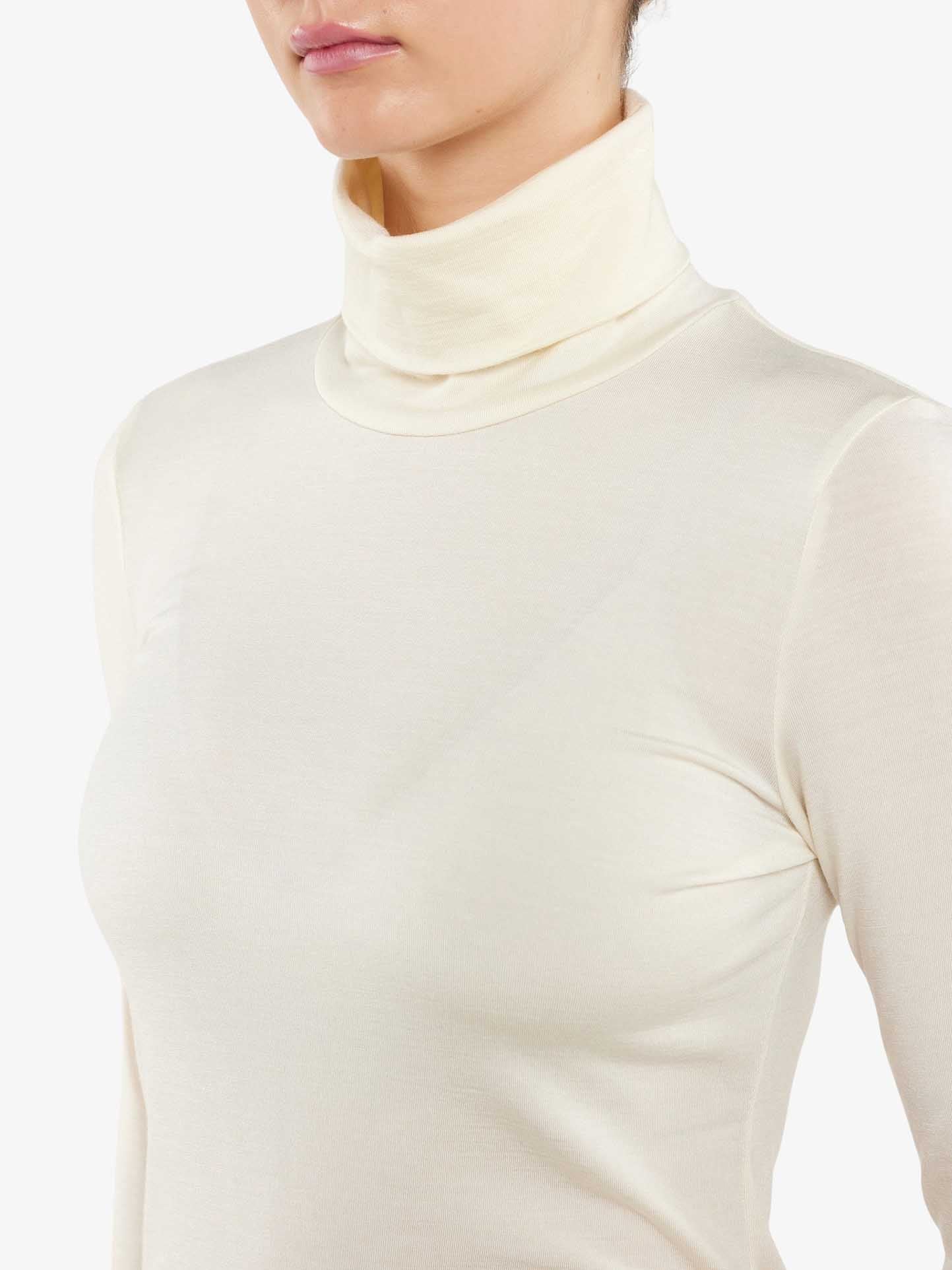 Person wearing a Hygge Turtleneck Women by We Norwegians in an ivory color, crafted from merino wool. The image focuses on the upper torso and neck, highlighting the smooth texture and fit of this luxury base layer. The background is plain white.