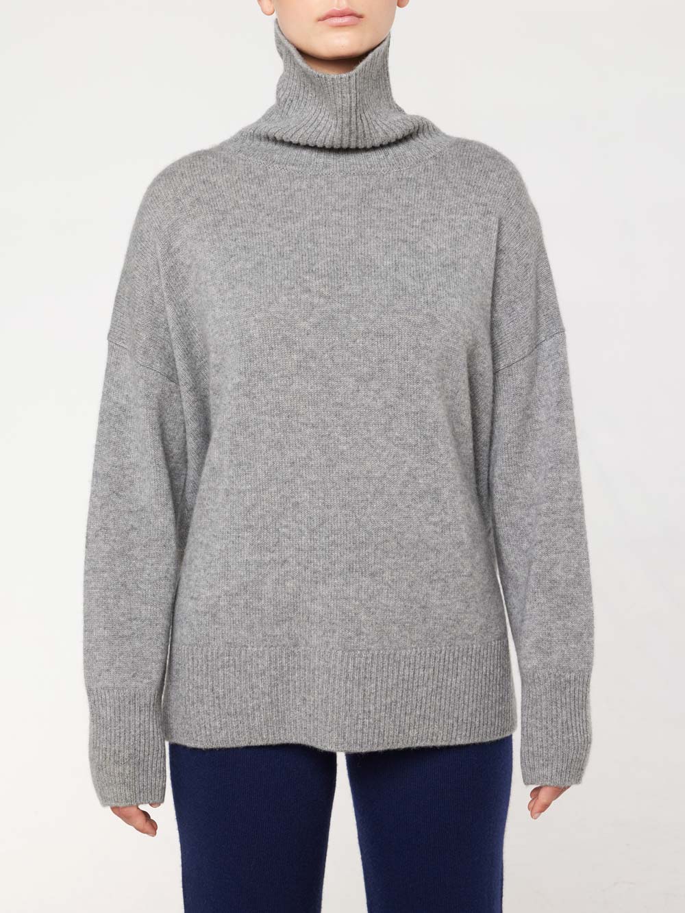 Wearing the We Norwegians Blefjell Cashmere Sweater in gray with long sleeves, ribbed hem, and cuffs, paired with dark pants against a plain white background. This sweater epitomizes timeless style.