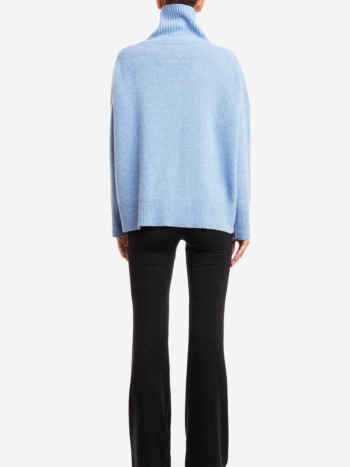 A person wearing the Blefjell Cashmere Sweater Women by We Norwegians, a light blue loose-fitting cashmere piece with long sleeves, stands timelessly with their back to the camera against a white backdrop, embodying effortless luxury fashion.