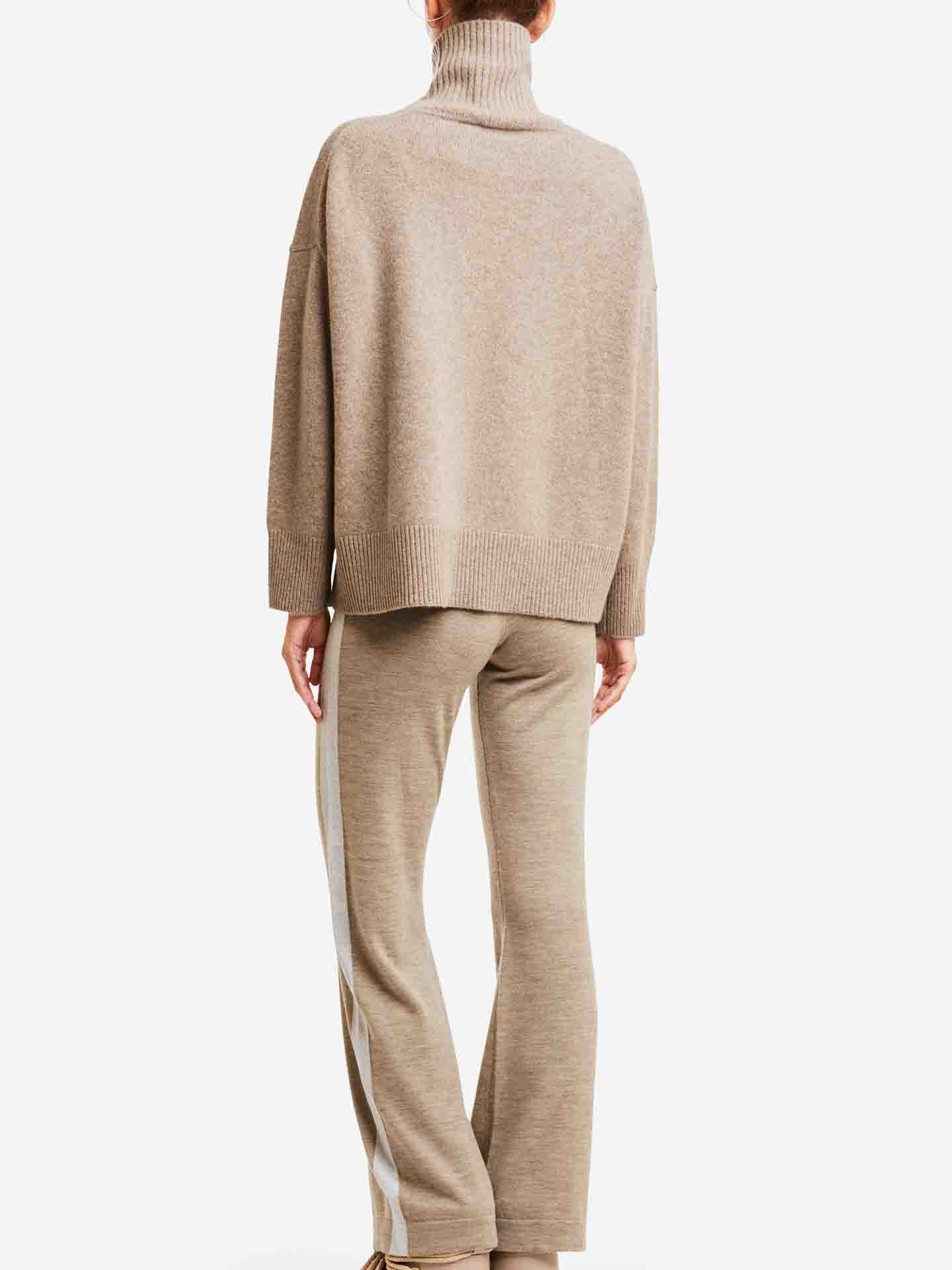 A person is shown from the back wearing We Norwegians' Blefjell Cashmere Sweater in beige with matching pants featuring white side stripes, all set against a plain white background. This luxury ensemble combines cozy comfort with a timeless style.