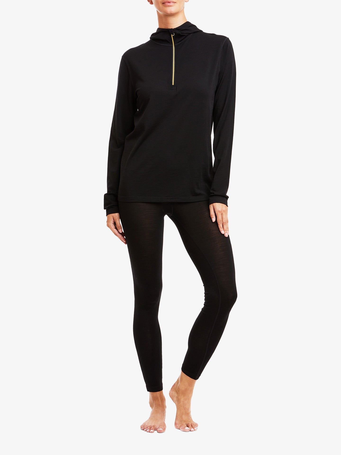 A person in Sno Merino Leggings Women by We Norwegians and a long-sleeve black top with a gold zipper at the neck, crafted from breathable fabric, stands against a plain white background. The person's hands rest at their sides, and they are barefoot.