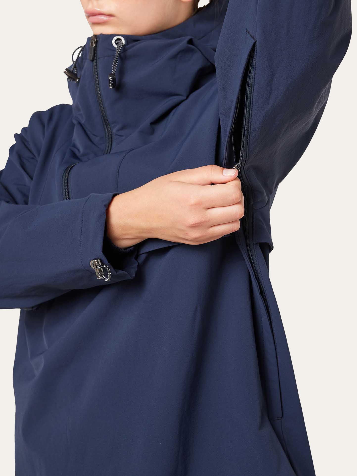 A woman wearing the Beito Anorak Women by We Norwegians unzips an underarm vent, highlighting the jacket’s functional design and adjustable features inspired by Norwegian outdoor style.