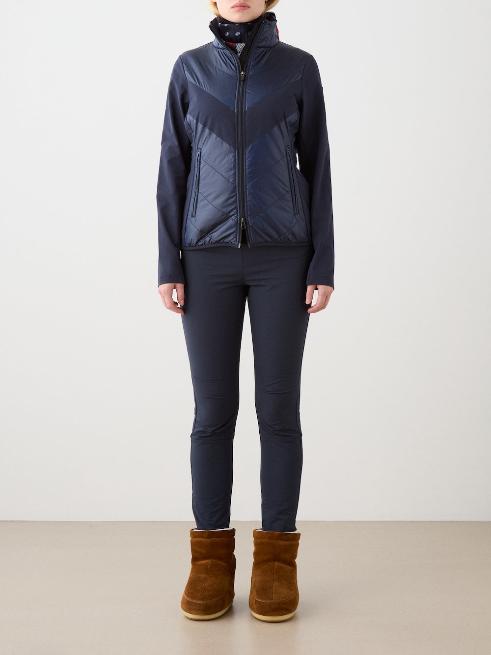 A person stands facing forward against a plain, light background, wearing the We Norwegians Beito Jacket Women in navy blue, paired with matching fitted pants and brown suede boots.