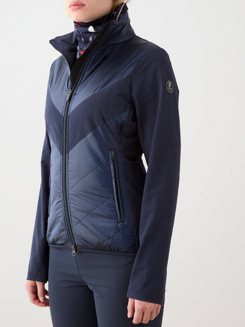 A woman models the We Norwegians Beito Jacket Women in dark blue, featuring a high collar and two zippered pockets, standing against a plain light background with only her torso and lower face visible.
