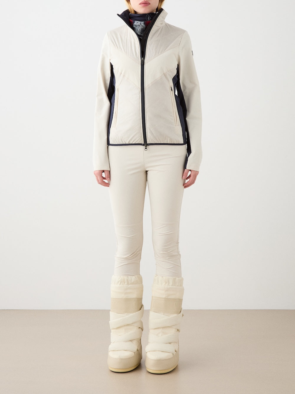 A person stands against a plain background wearing the Beito Jacket Women by We Norwegians, featuring a cream color and water repellent finish, styled with matching pants and beige snow boots—perfect for winter or snow activities.