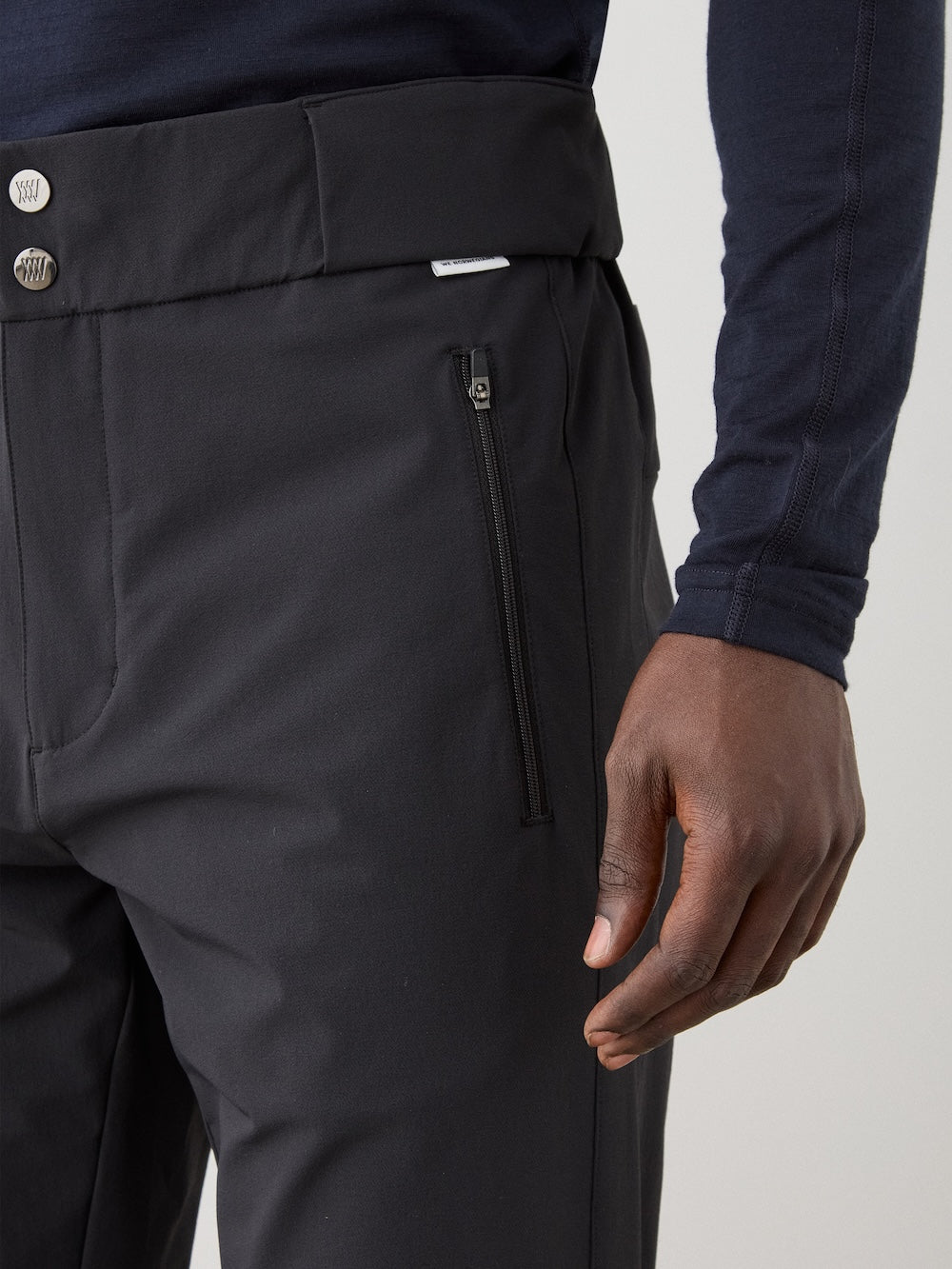 A person wearing We Norwegians Beito Pant Men, featuring a front zipper pocket, paired with a dark long-sleeve shirt and showing their right hand resting by their side.