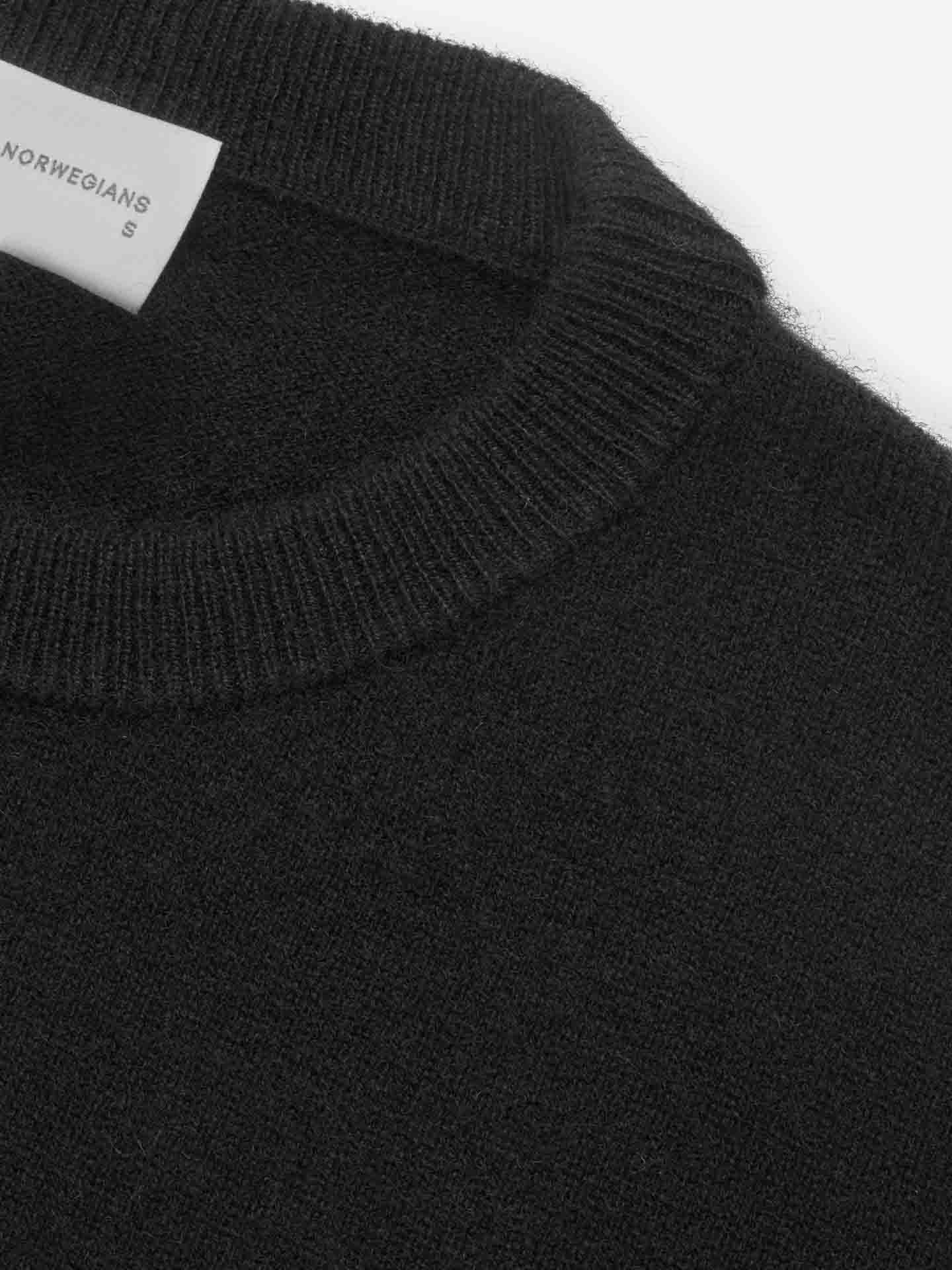 Close-up image of a black, round-neck sweater made of soft, knit fabric. A white label with the text "We Norwegians" and "S" is partially visible against the inner neckline. This luxurious staple, part of the Blefjell Cashmere Crewneck Women series by We Norwegians, adds pure cashmere elegance to any wardrobe.
