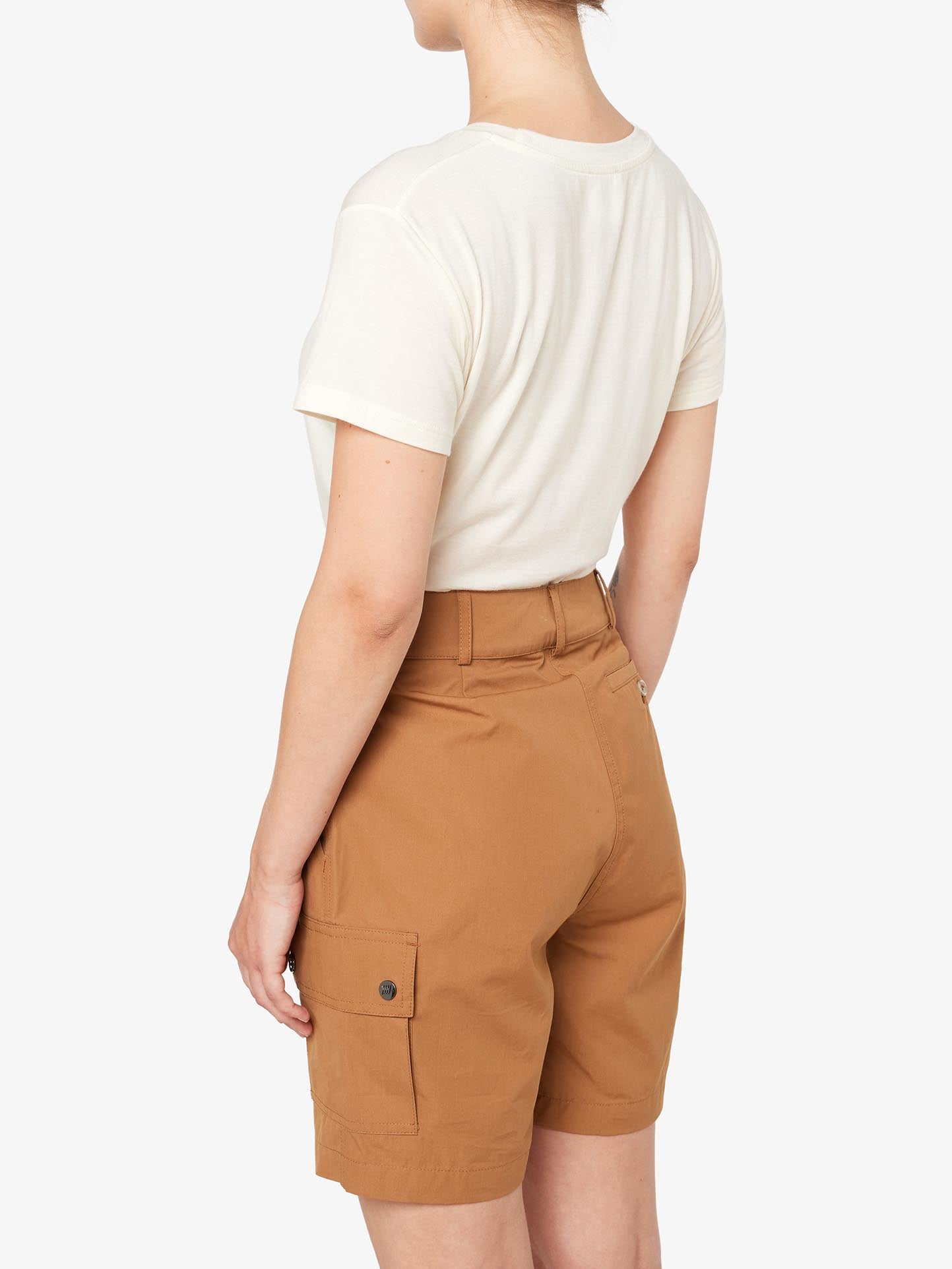 A person with light skin and short hair is seen from behind, wearing a white Ventile® fabric t-shirt and high-waisted We Norwegians Lyngen Shorts Women in Cinnamon, featuring a pocket on the side. Ideal for outdoor enthusiasts, this outfit not only looks stylish but also boasts weatherproof qualities. The background is white.