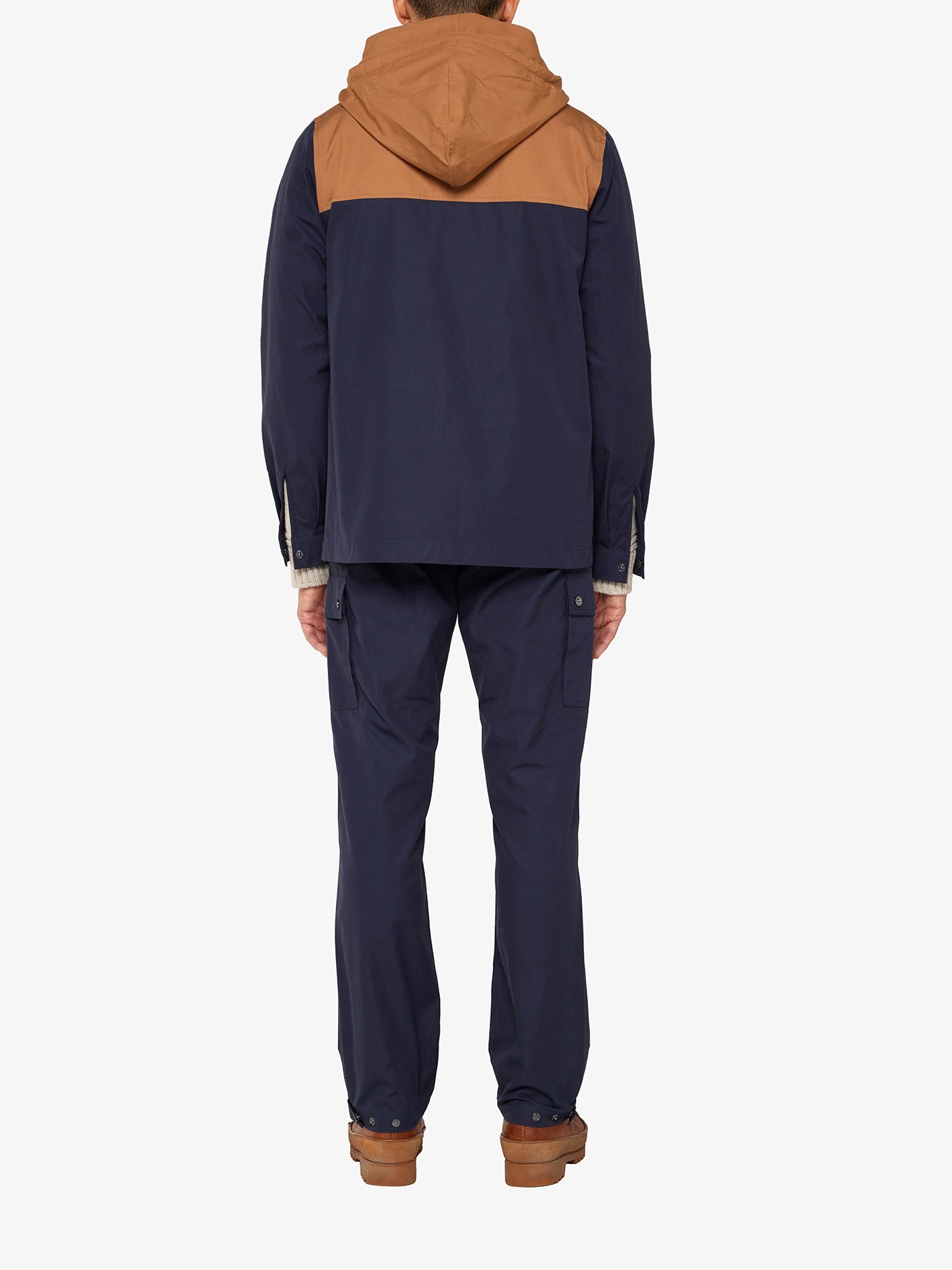 An outdoor enthusiast, wearing We Norwegians' Lyngen Jacket Men in dark blue with Ventile® cotton, stands against a plain white background. He pairs it with navy pants and brown shoes.
