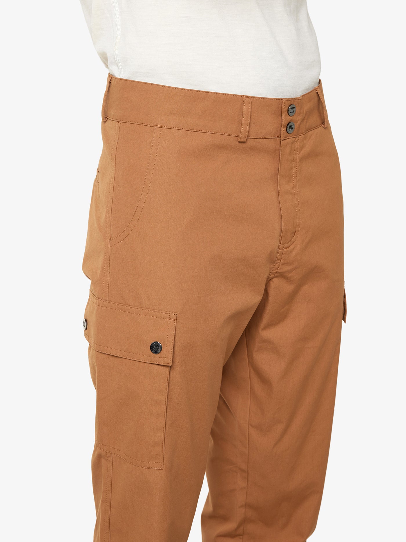 Close-up of a person wearing the We Norwegians Lyngen Pant Men in Cinnamon, paired with a white top. These light brown cargo pants are made from thin, breathable Ventile® cotton fabric and feature several pockets, including a side pocket with a button closure. The shot highlights the waist down to the mid-thigh and showcases the ideal apparel choice for outdoor enthusiasts.