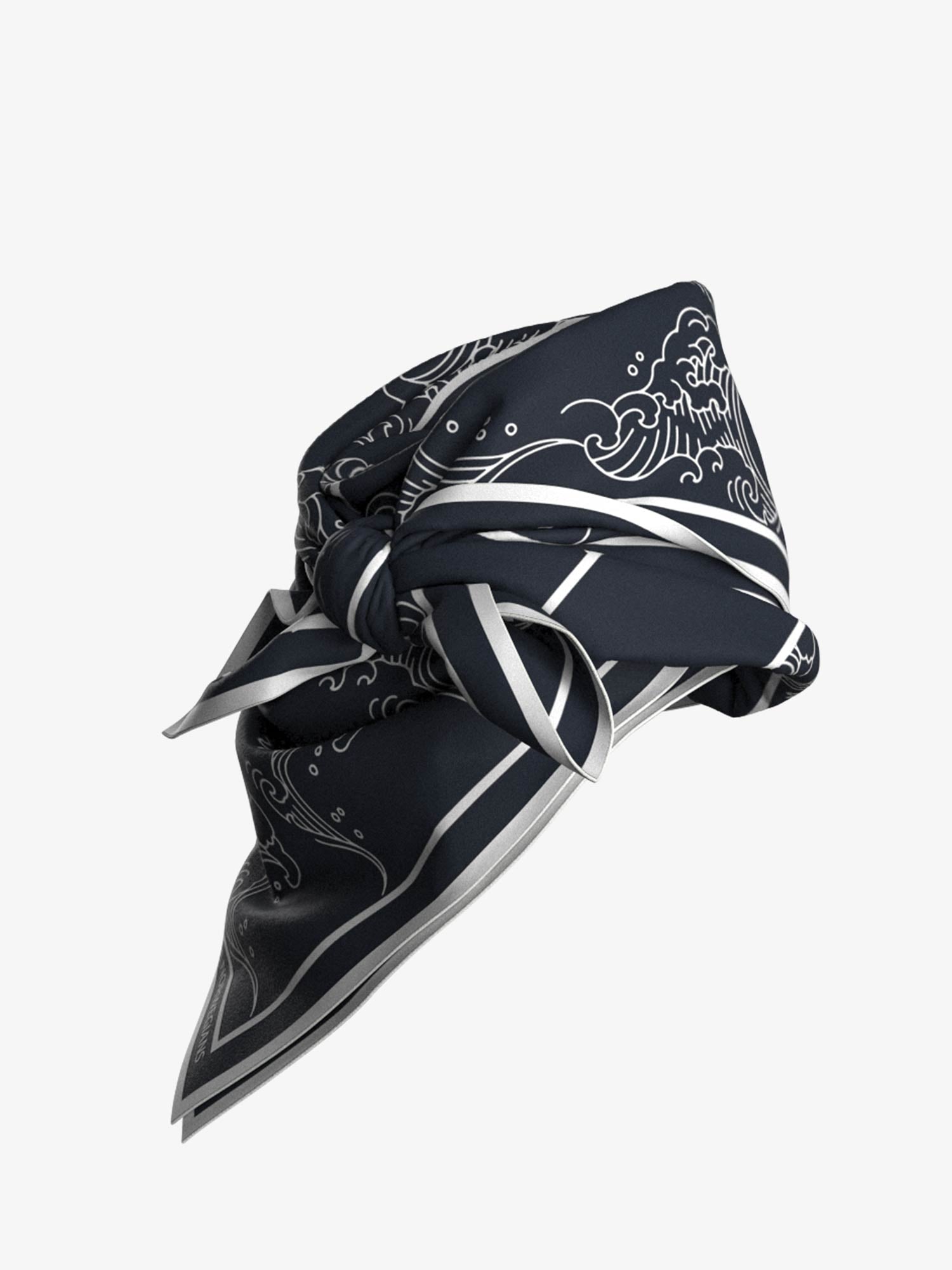 A We Norwegians Wavy Silk Scarf in navy blue, featuring intricate white wave patterns that are reminiscent of Ukiyo-e art, is neatly tied into a knot. The scarf's edges have a thin white border, adding an elegant touch to its design. Set against a plain white background, the detailed pattern and texture of the scarf are highlighted beautifully.