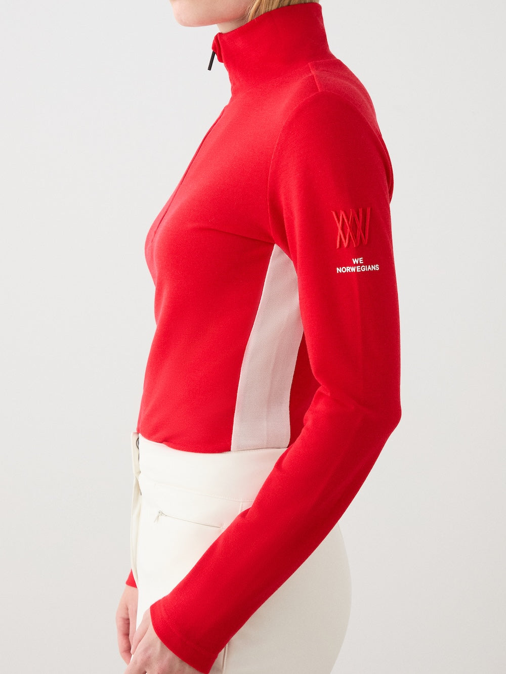 We Norwegians | FW25 | Womens Voss 1/4-Zip_Red | Model is wearing this light knit top with a stand collar, 1/4th zipper opening and long sleeves - paired with white pants on an off-white background | Close-up