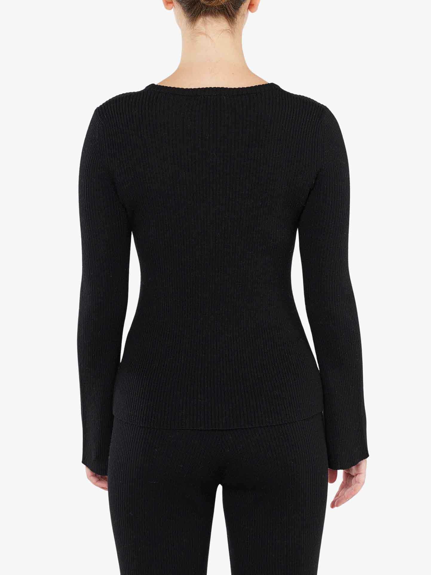 A person is standing facing away from the camera, wearing a black Geilo Ribbed Sweater Women by We Norwegians and matching pants. The background is plain white, and the person's hair is tied up.