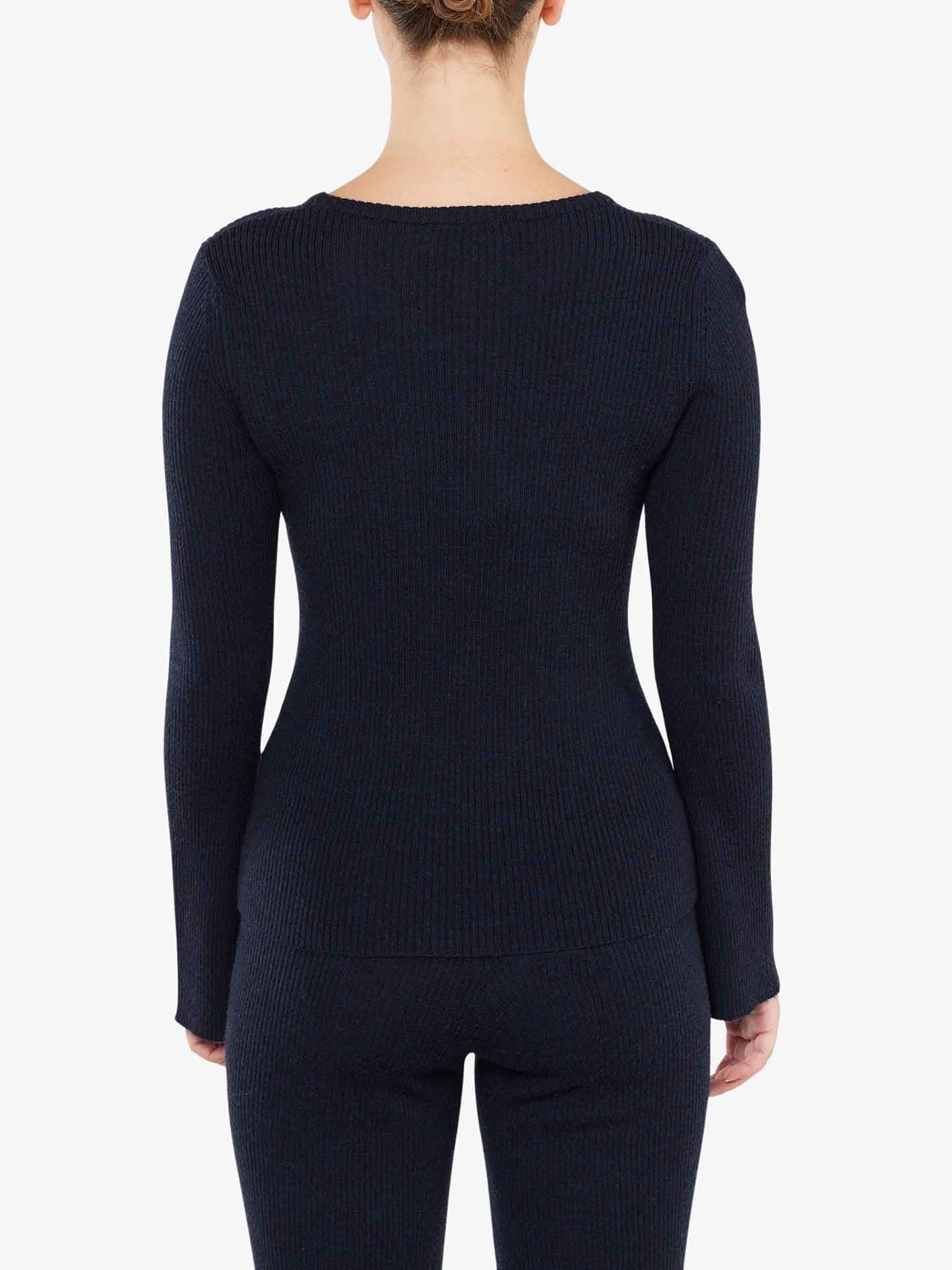 A person is shown from the back, wearing a fitted, long-sleeve Geilo Ribbed Sweater Women and matching pants from We Norwegians. The outfit has a ribbed texture and appears to be crafted from merino wool. The person's hair is tied up, and the background is plain white.