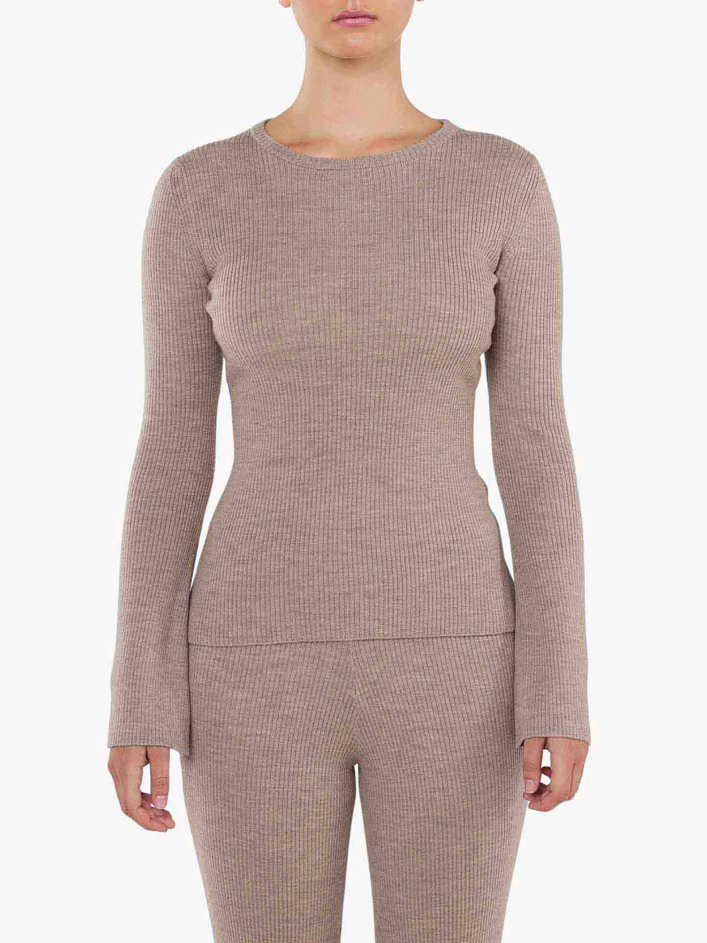 A person wearing the "Geilo Ribbed Sweater Women" from We Norwegians, featuring a form-fitting, long-sleeve beige ribbed-knit top and matching pants made from soft merino wool, against a plain white background. The outfit showcases a simple, minimalist design and the person's head is not fully visible in the image.