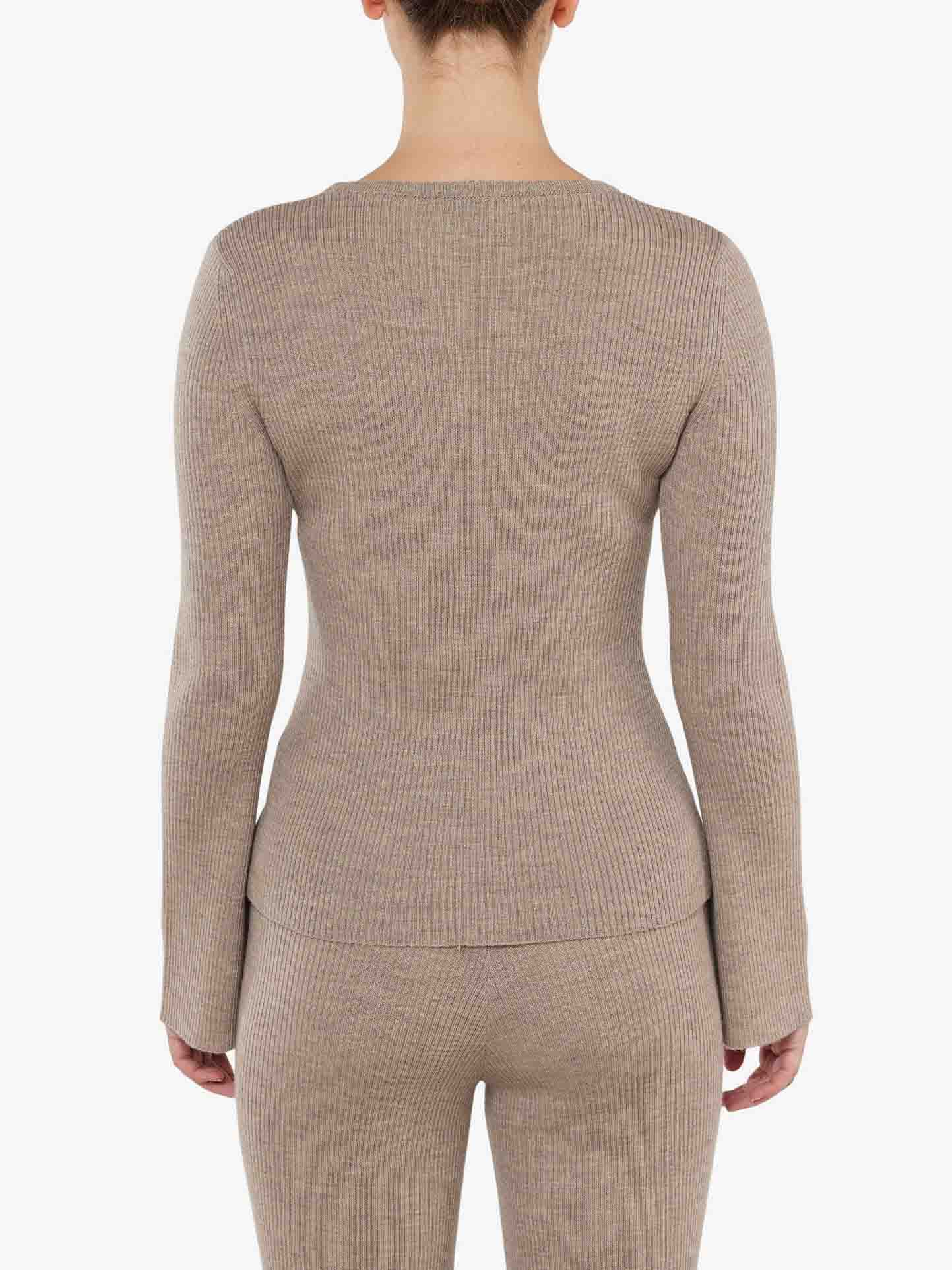 The image depicts a person standing with their back to the camera, wearing the Geilo Ribbed Sweater Women by We Norwegians, featuring fitted merino wool with trumpet sleeves, paired with matching bottoms. The background is plain white.
