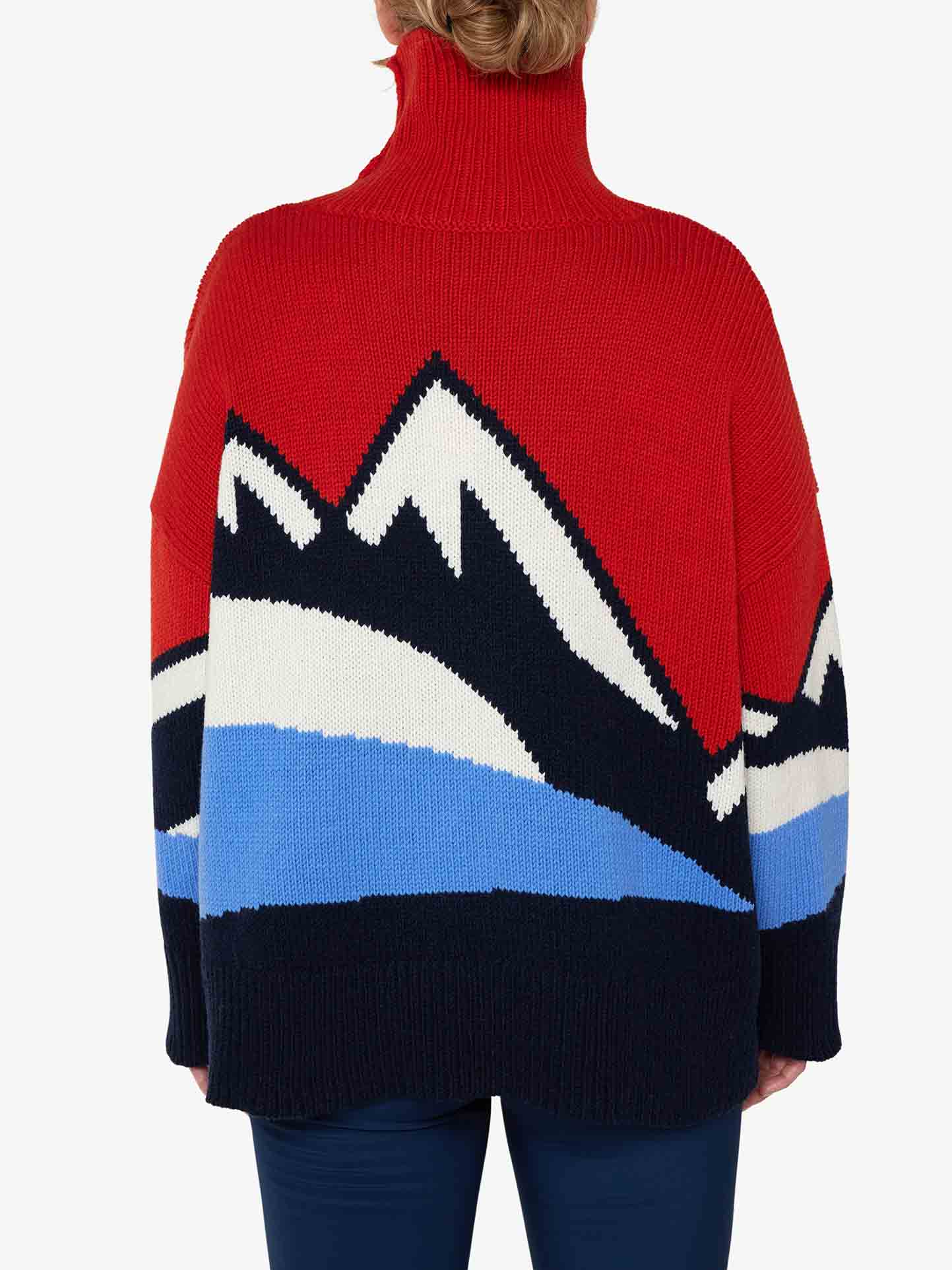 A person wearing the cozy We Norwegians Snowmountain Sweater Women, made from luxurious Merino wool, showcases a stunning color-blocked mountain range pattern in black, white, and blue on the back. The person's back is to the camera, perfectly highlighting this ideal piece of fall fashion.
