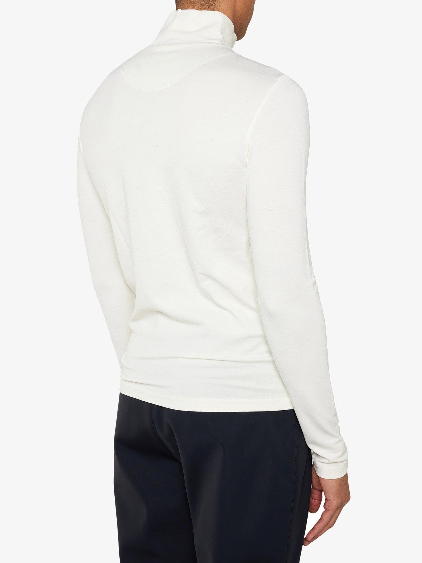A person wearing the Voss Chevron Zipup Men from We Norwegians, a long-sleeved white turtleneck sweater made of superfine Merino wool, paired with black pants, shown from the back. The outfit showcases a clean and minimalist design, with an emphasis on simplicity and elegance. The background is plain white.