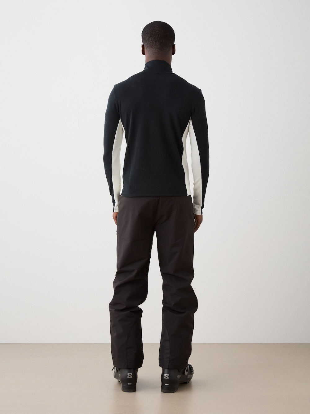 We Norwegians | FW25 | Mens Voss 1/4-Zip_Black | Model is wearing this light weight knitted top with a stand collare, 1/4th zipper opening and long sleeves - paired with black pants on an off-white background | Back