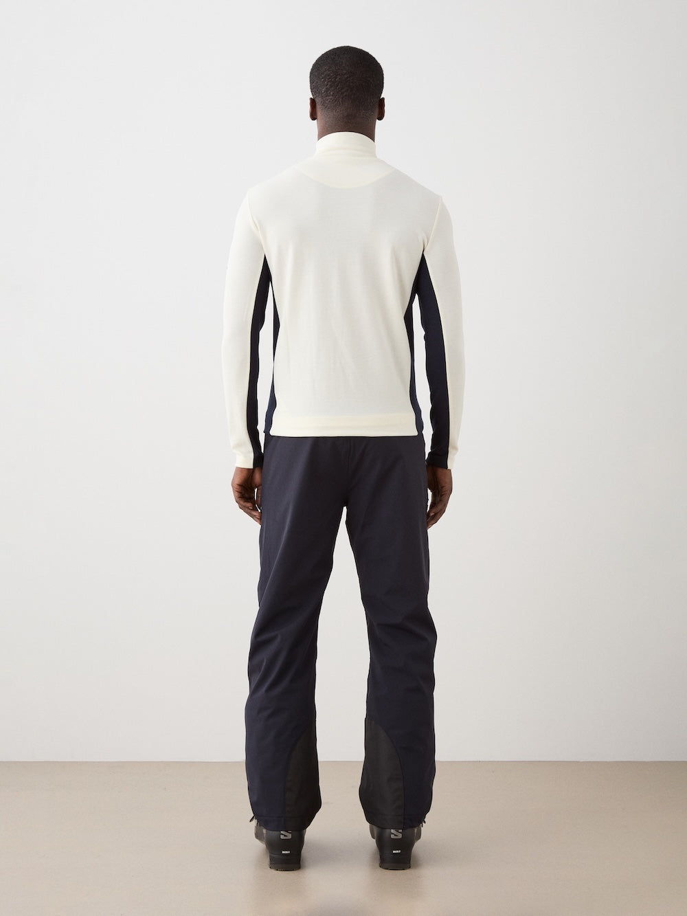 We Norwegians | FW25 | Mens Voss 1/4-Zip_Off white | Model is wearing this light weight knitted top with a stand collare, 1/4th zipper opening and long sleeves - paired with black pants on an off-white background | Back