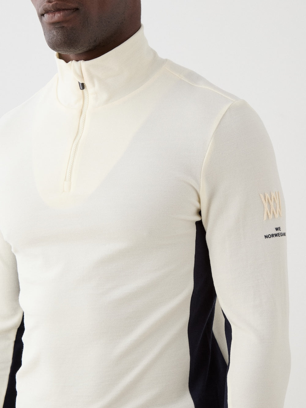 We Norwegians | FW25 | Mens Voss 1/4-Zip_Off white | Model is wearing this light weight knitted top with a stand collare, 1/4th zipper opening and long sleeves on an off-white background | Close-up