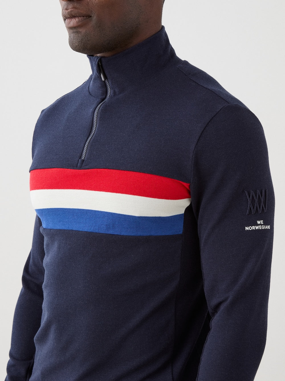 A man wearing the We Norwegians Ski 1/4-Zip Men sweater in navy blue, featuring red, white, and blue chest stripes and "WE NORWEGIANS" text on the left sleeve.