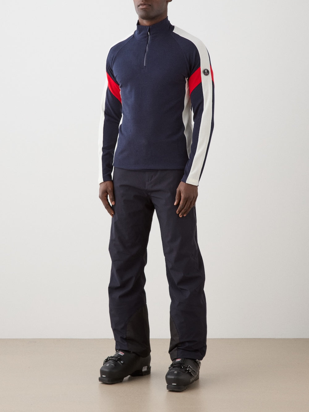 The We Norwegians Zermatt Zipup Men is a navy long-sleeve ski sweater with a quarter-zip, white shoulder and sleeve panels, red diagonal stripes on the upper sleeves, and a small circular logo patch on the left upper arm | Front