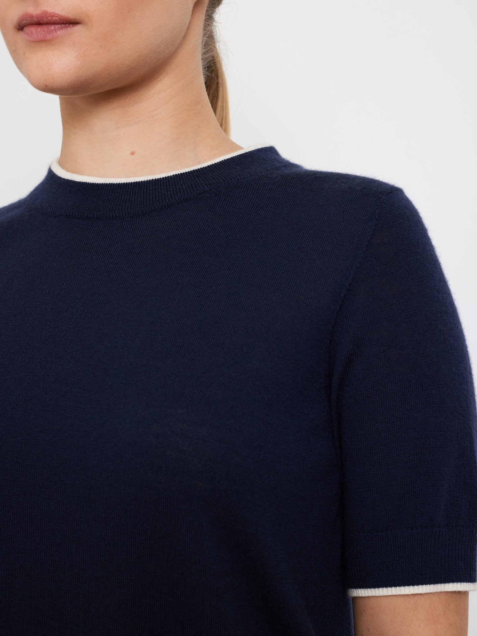 A person is wearing the We Norwegians "Club Top Women," a navy short-sleeved shirt with fine white trim on the collar in a relaxed fit, against a plain white background.