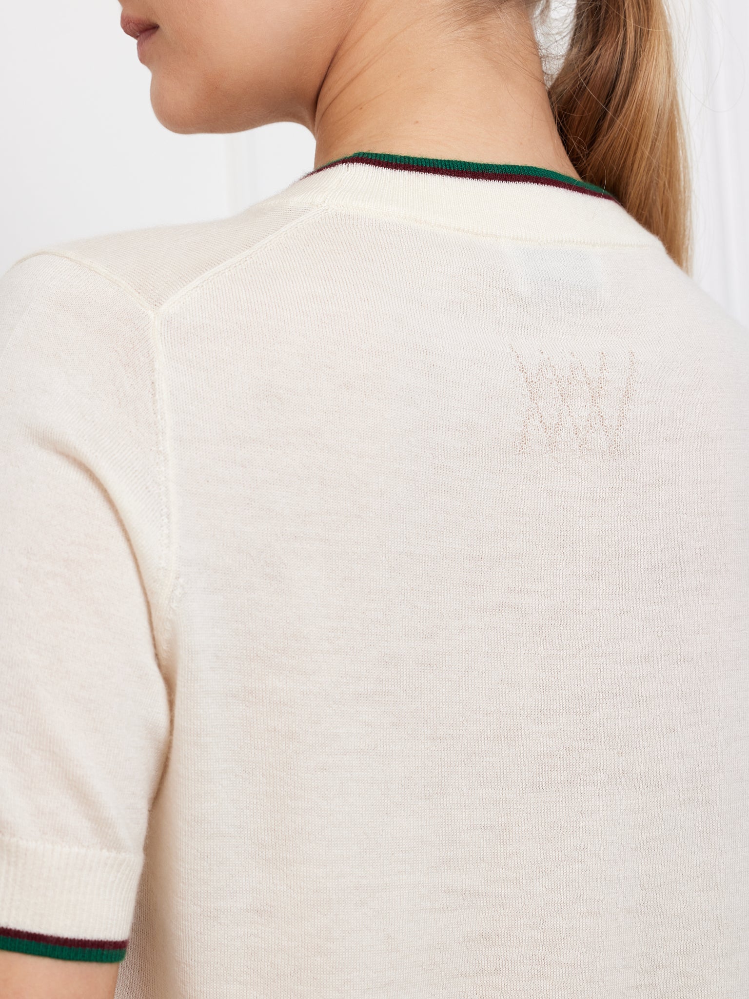 With long hair, a person is seen from the back wearing the Club Top Women by We Norwegians, a cream-colored short sleeve shirt. This relaxed-fit piece combines comfort and elegance with a subtle embroidered style stitched near the neckline.