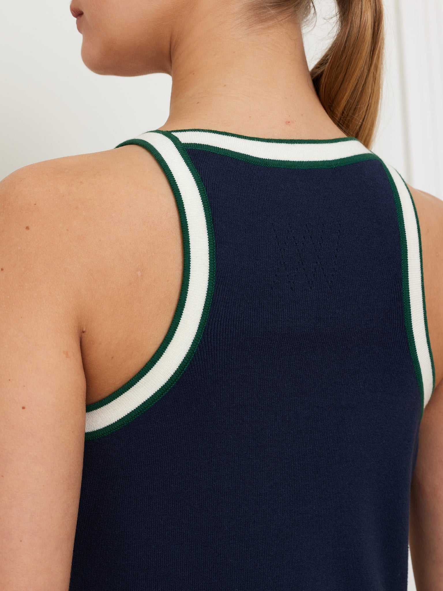 A person models the We Norwegians "Team Dress Women," showcasing its navy blue color with green and white trim. They sport a ponytail, revealing the racerback design with a textured pattern on the upper back.