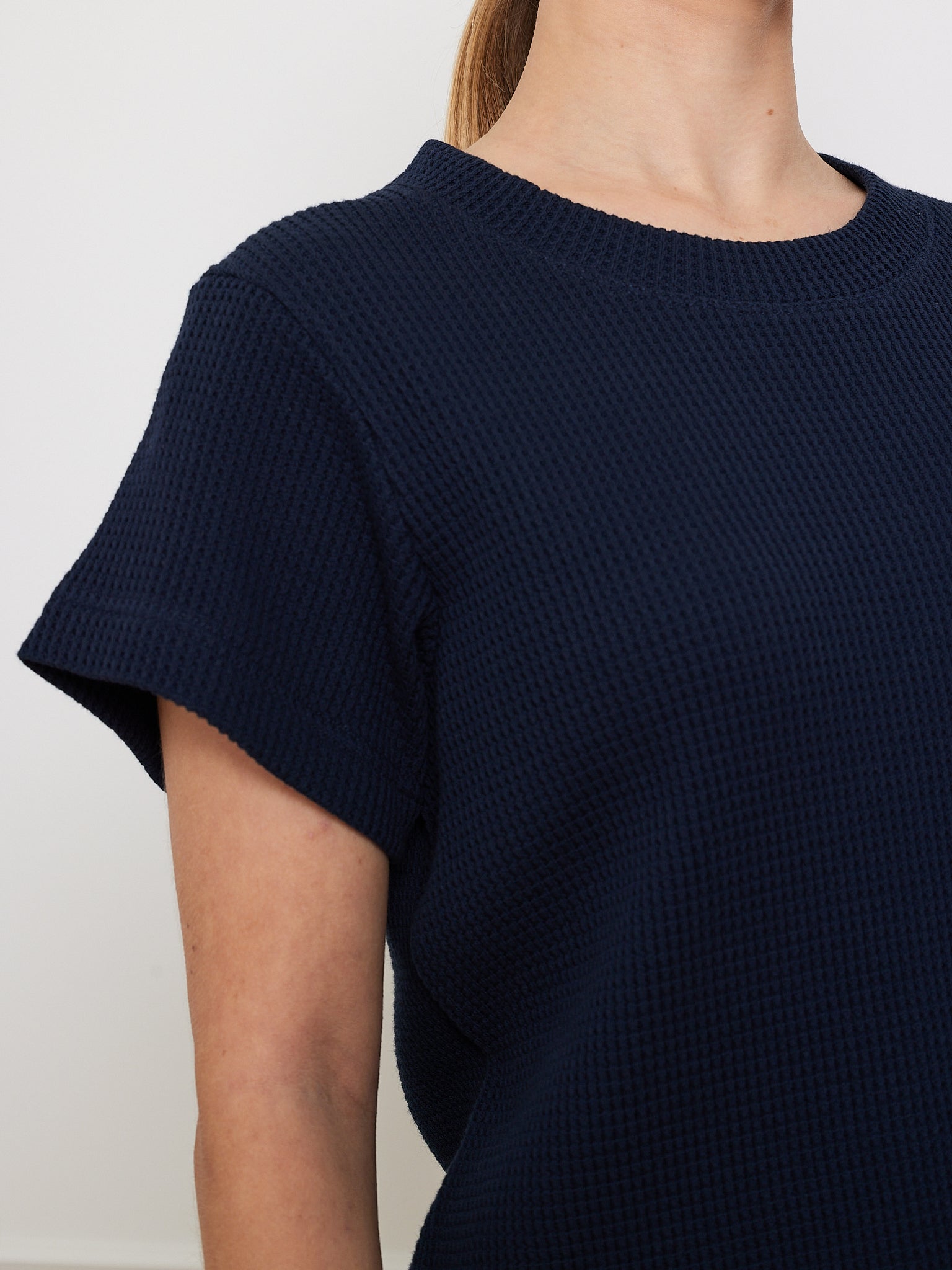 An individual dons the We Norwegians Waffle Tee Women in navy blue, ideal as a wardrobe staple. The shot highlights the upper torso and shoulder against a plain white background, with the head partially visible but facial features obscured.
