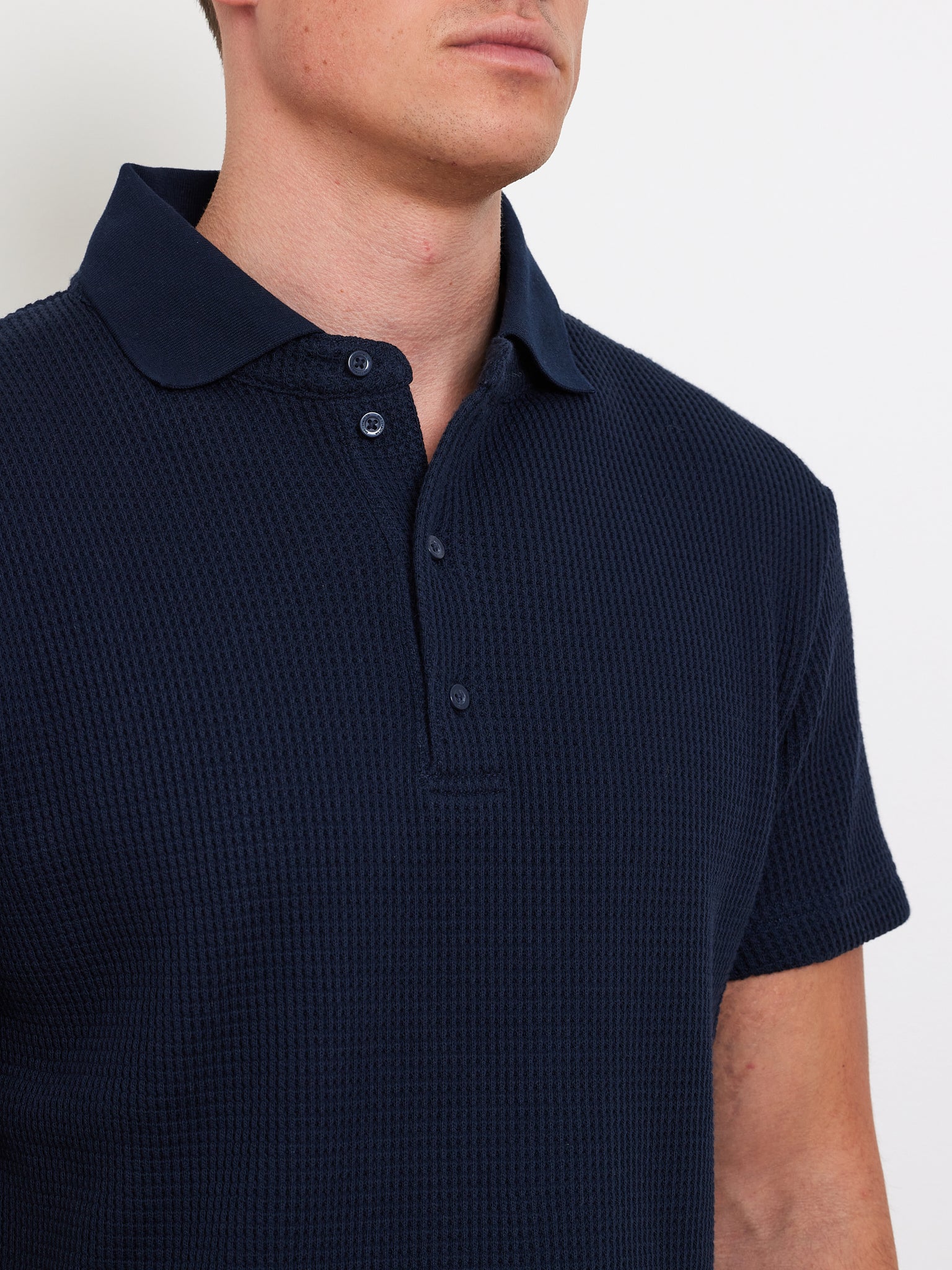 A person models the We Norwegians Waffle Polo Men, a dark navy textured shirt with a relaxed fit and button-up collar, against a white background, facing slightly to the right.