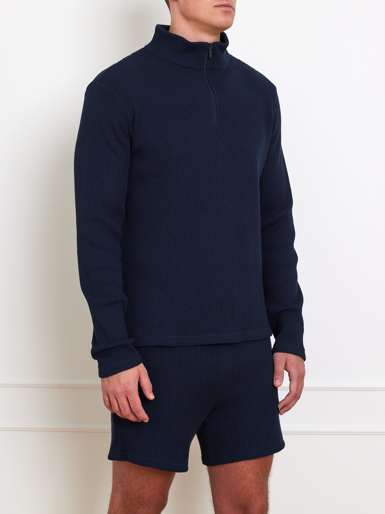 A person models the We Norwegians Waffle Sweater Men, a relaxed-fit 100% cotton navy piece, with matching navy shorts against a plain white background, head not visible.